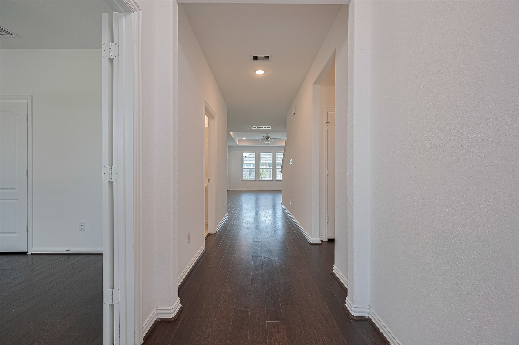 Bright, open hallway with dark wood floors leading to a spacious living area. Bright, open hallway with dark wood floors leading to a spacious living area.