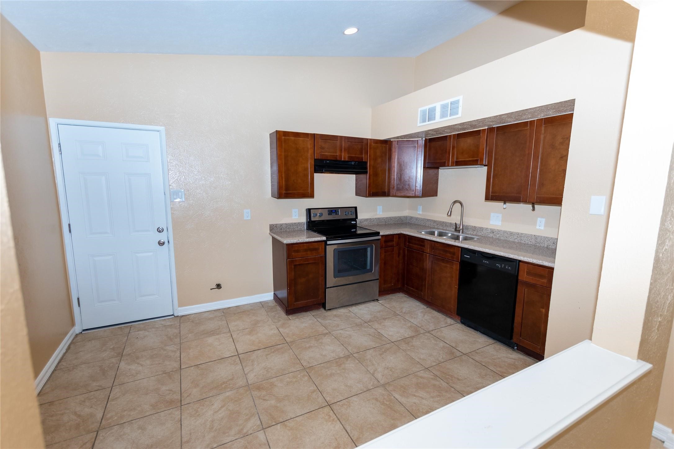 Modern kitchen with stainless steel appliances, rich wood cabinetry, and tile flooring, offering a spacious and functional layout.