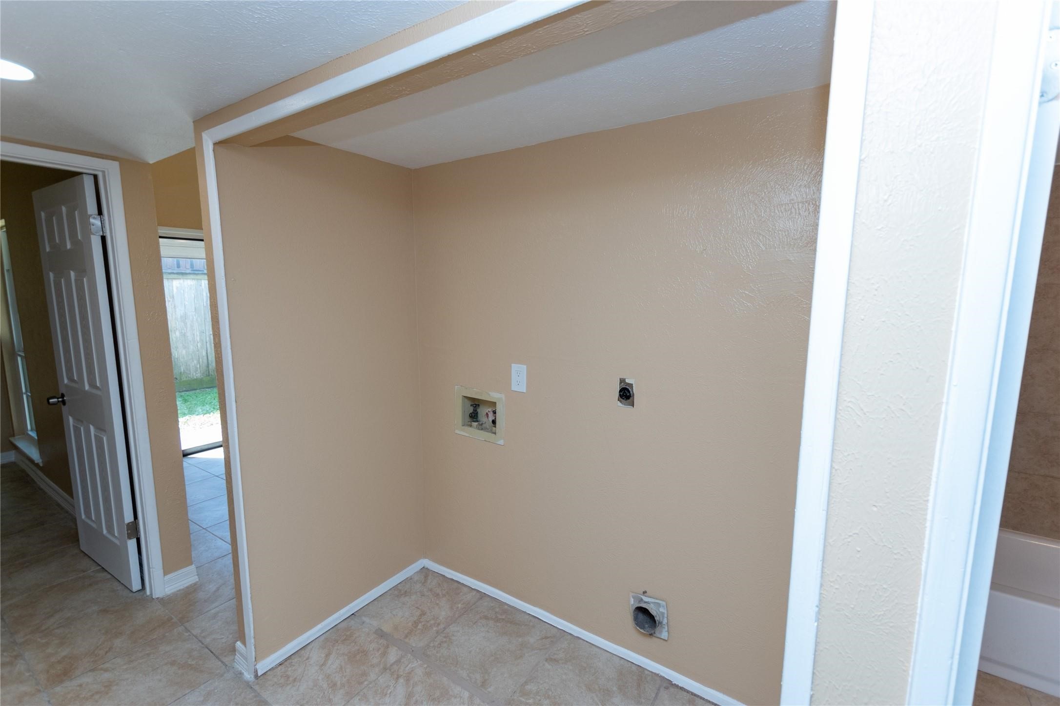 Convenient laundry nook with washer and dryer hookups, featuring neutral walls and easy-to-clean tile flooring.