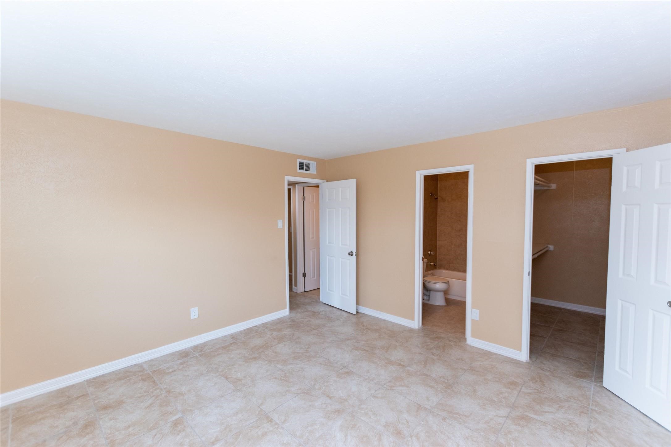 Spacious bedroom with neutral tones, featuring tiled flooring, an en-suite bathroom, and a walk-in closet.