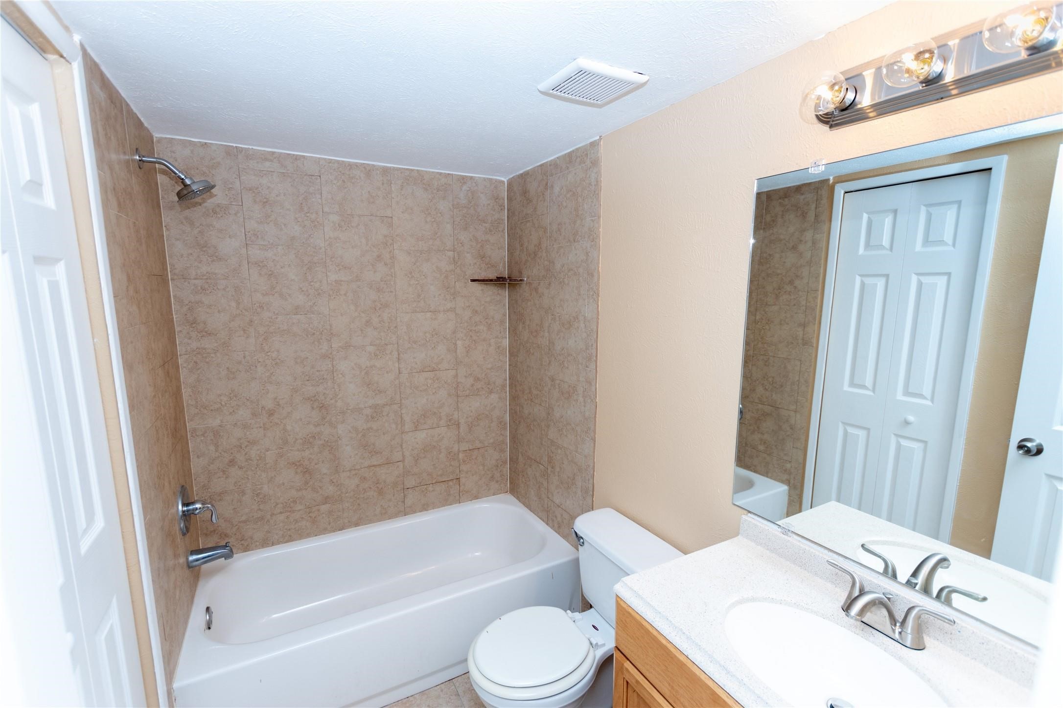 Charming bathroom featuring a tiled shower-tub combo, a sleek vanity with a modern faucet, and a large mirror enhancing the sense of space.