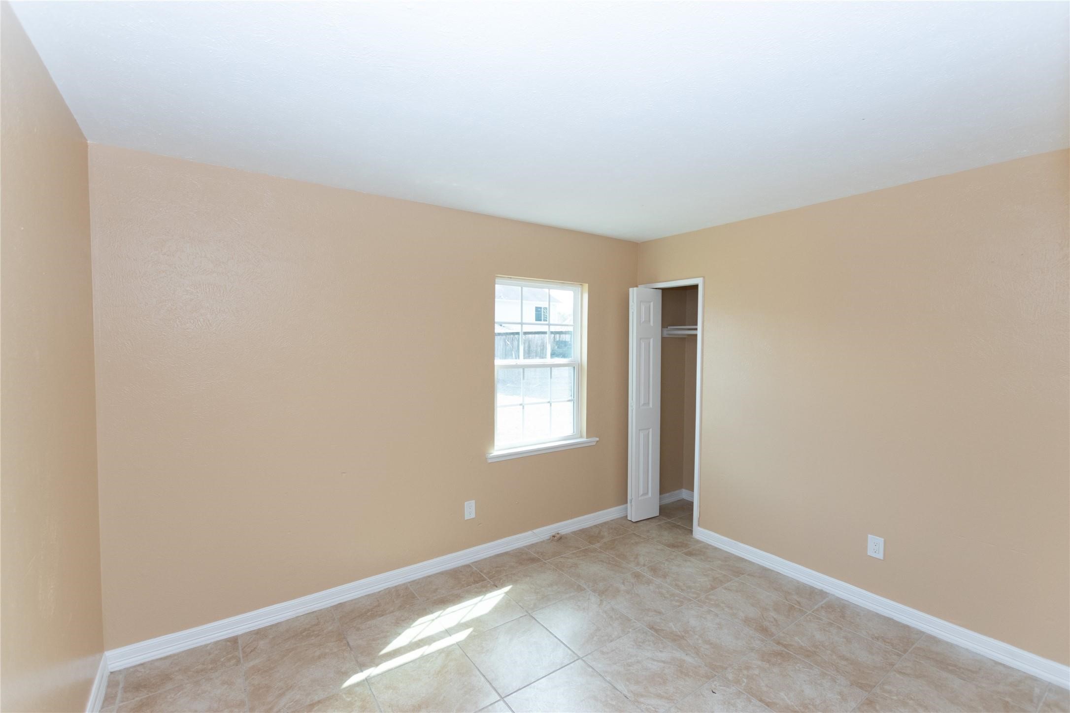 Bright and inviting room with neutral walls, a window for natural light, and a convenient closet, perfect for customization.