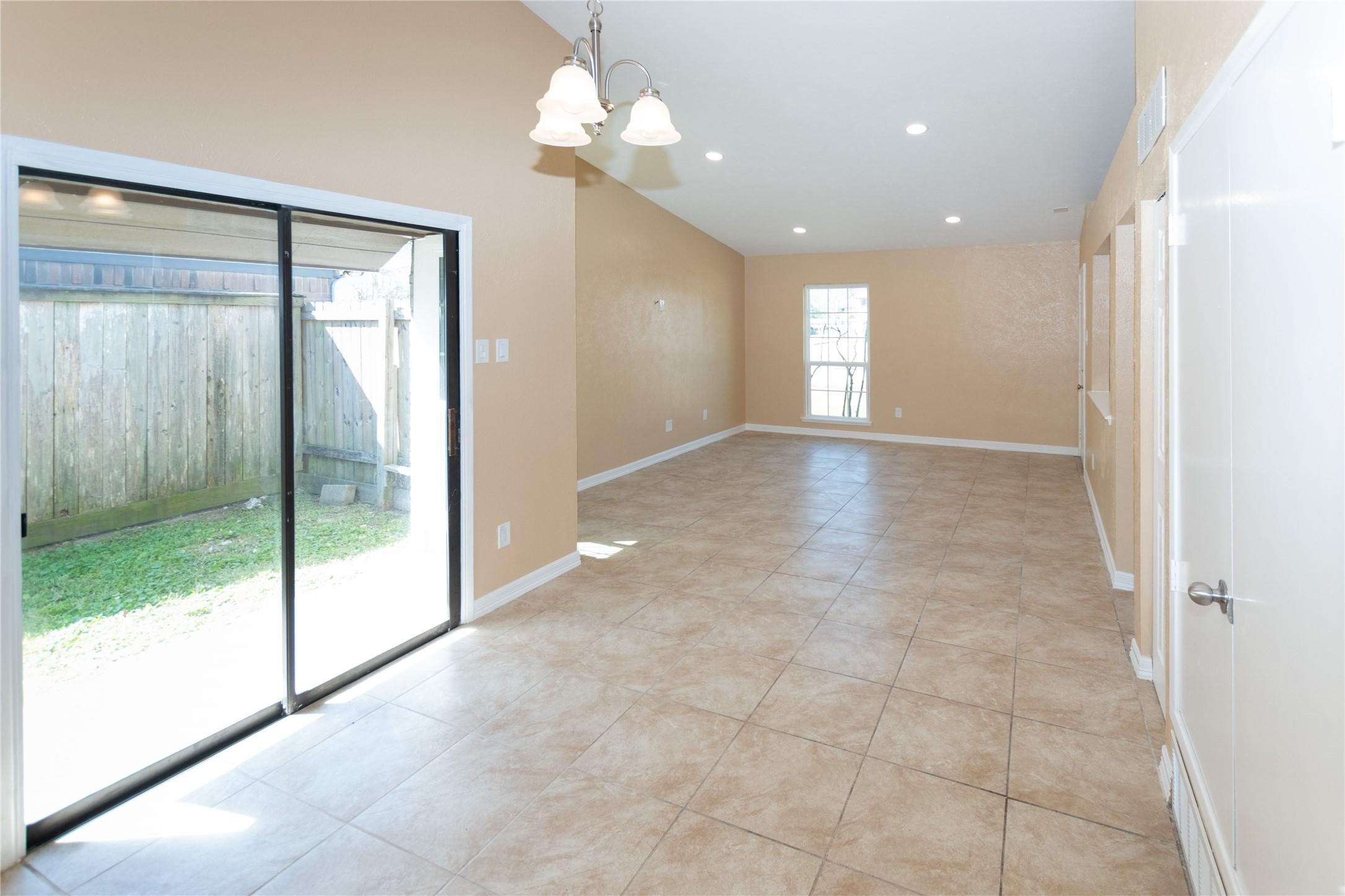 Bright and spacious open-plan living area featuring large tile flooring, recessed lighting, and abundant natural light from sliding glass doors leading to the backyard.