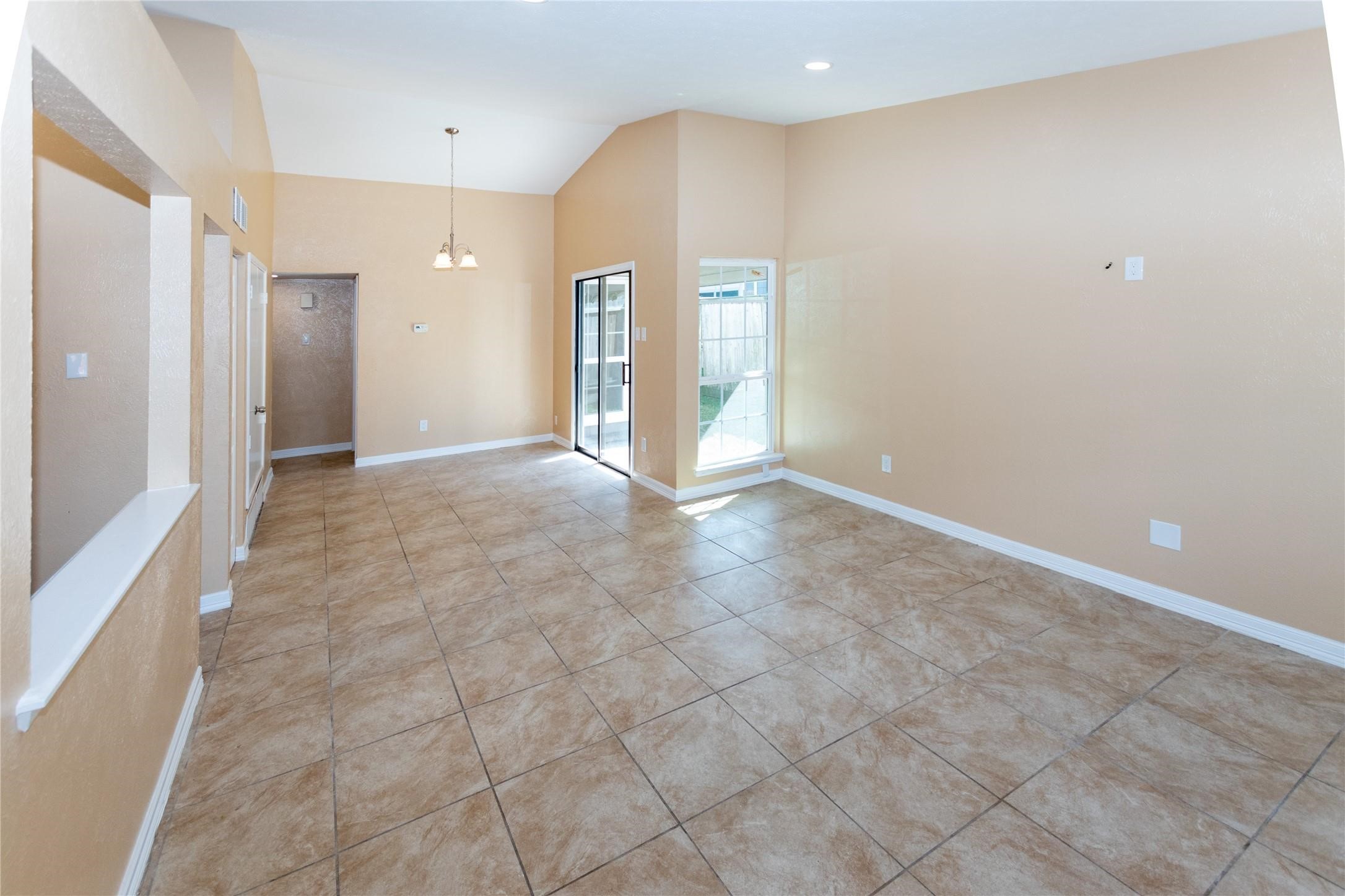 Spacious living area with high ceilings, tile flooring, and abundant natural light from large windows and a glass door leading to the backyard.
