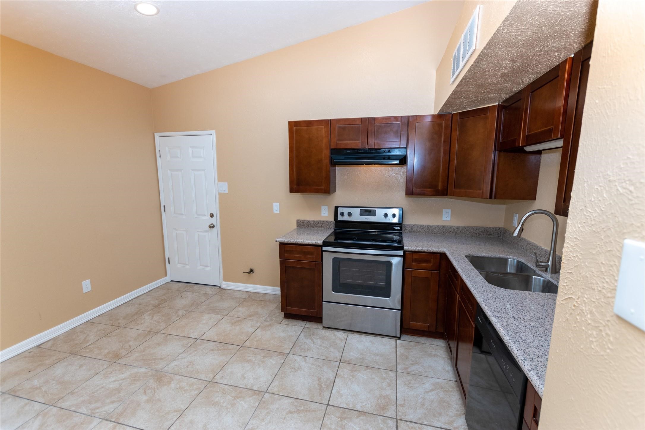 Modern kitchen with rich wood cabinetry, stainless steel appliances, and a sleek countertop, complemented by tiled flooring and warm wall tones.