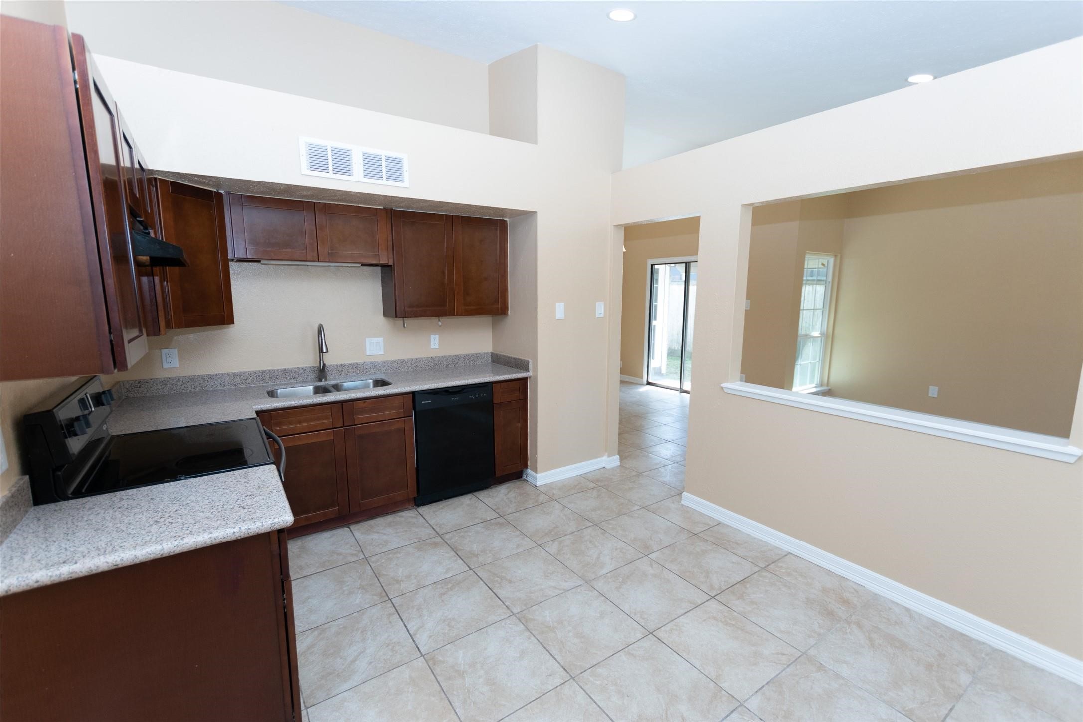 Bright kitchen with dark wood cabinetry, sleek granite countertops, and modern appliances, opening to a spacious living area through a convenient pass-through window.