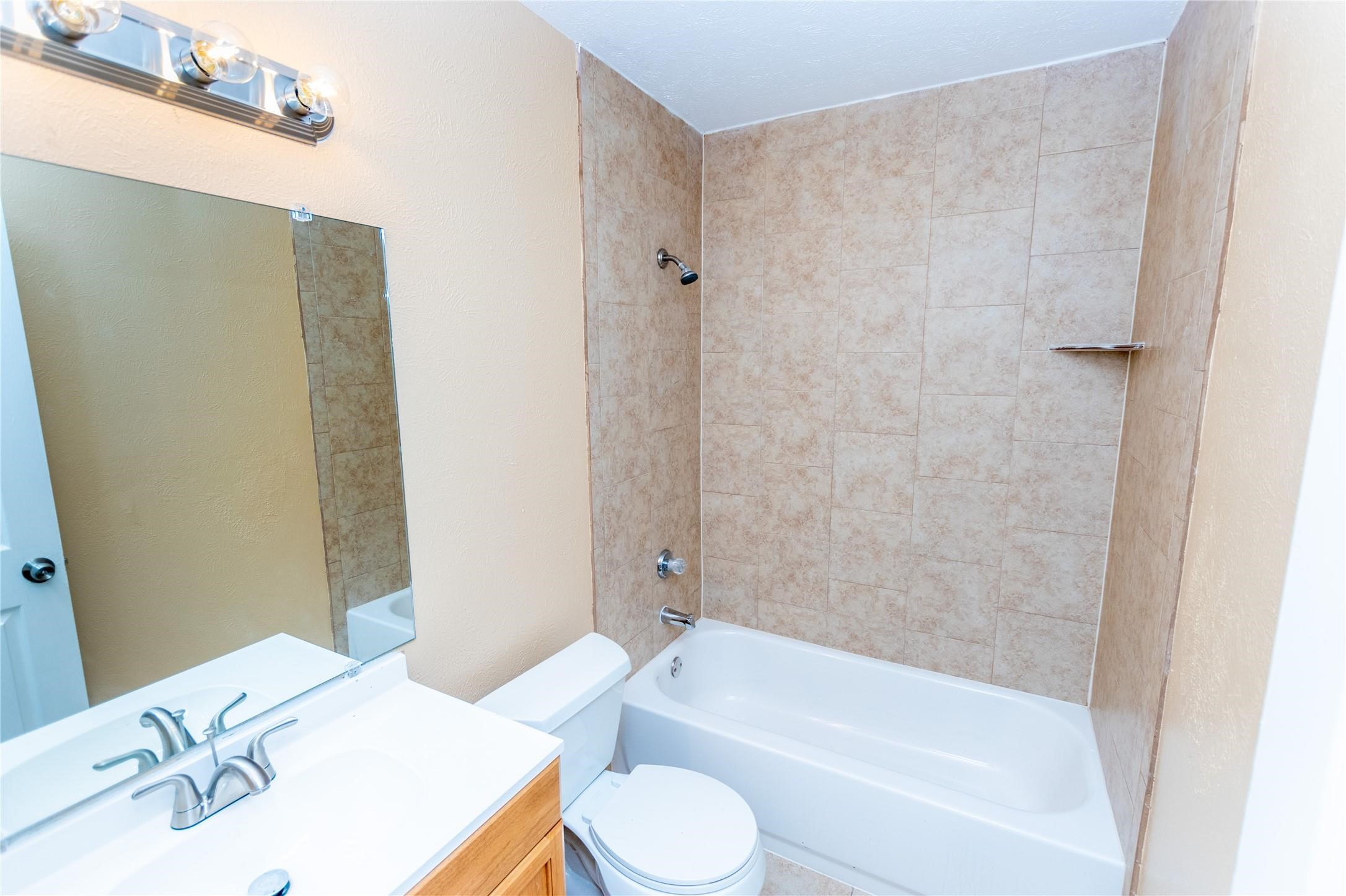 Bright bathroom with a tiled shower-tub combo, sleek vanity, and modern lighting.