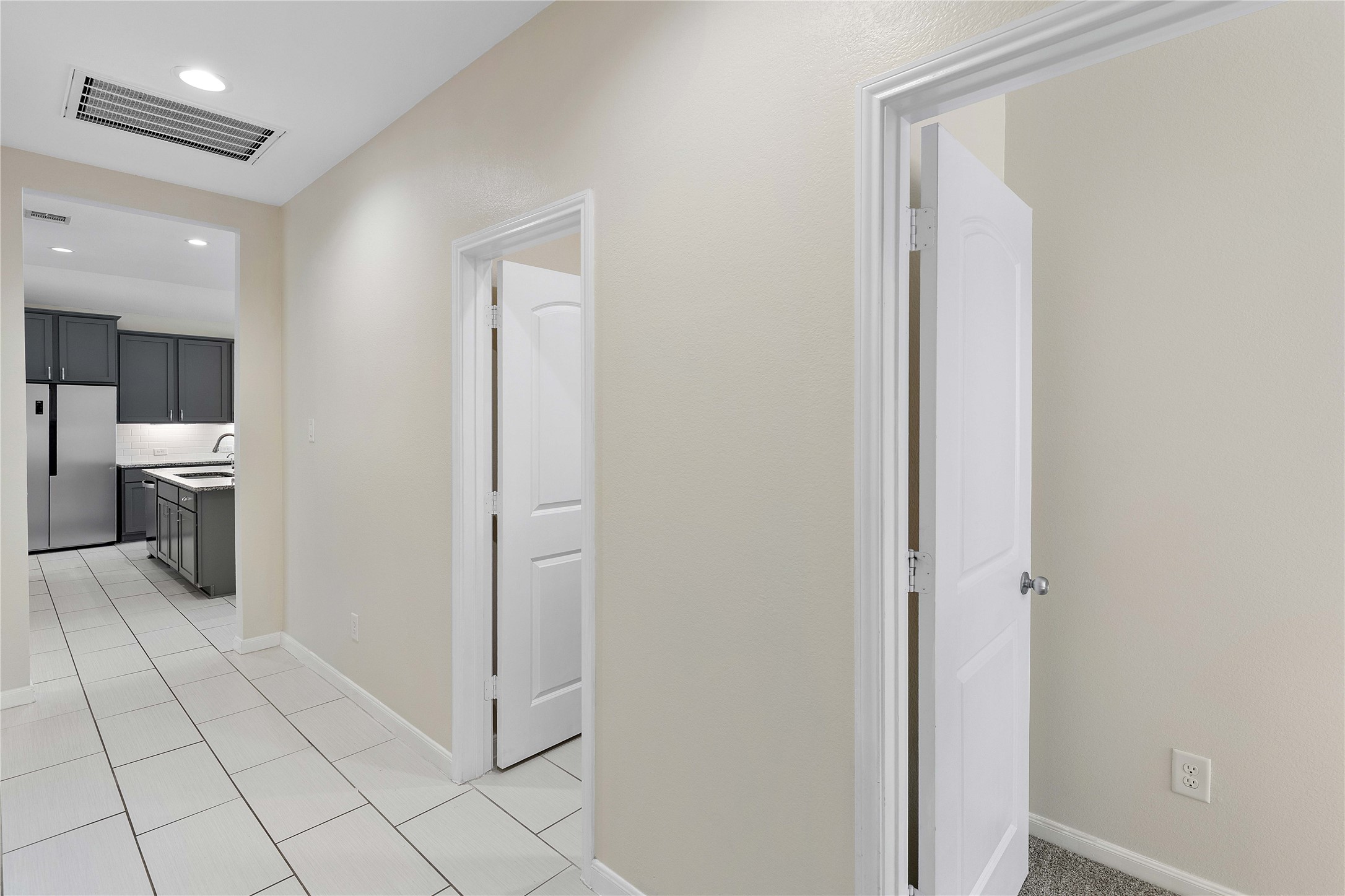 Bright hallway leads to a modern kitchen featuring sleek gray cabinetry and stainless steel appliances, offering a functional and stylish space.