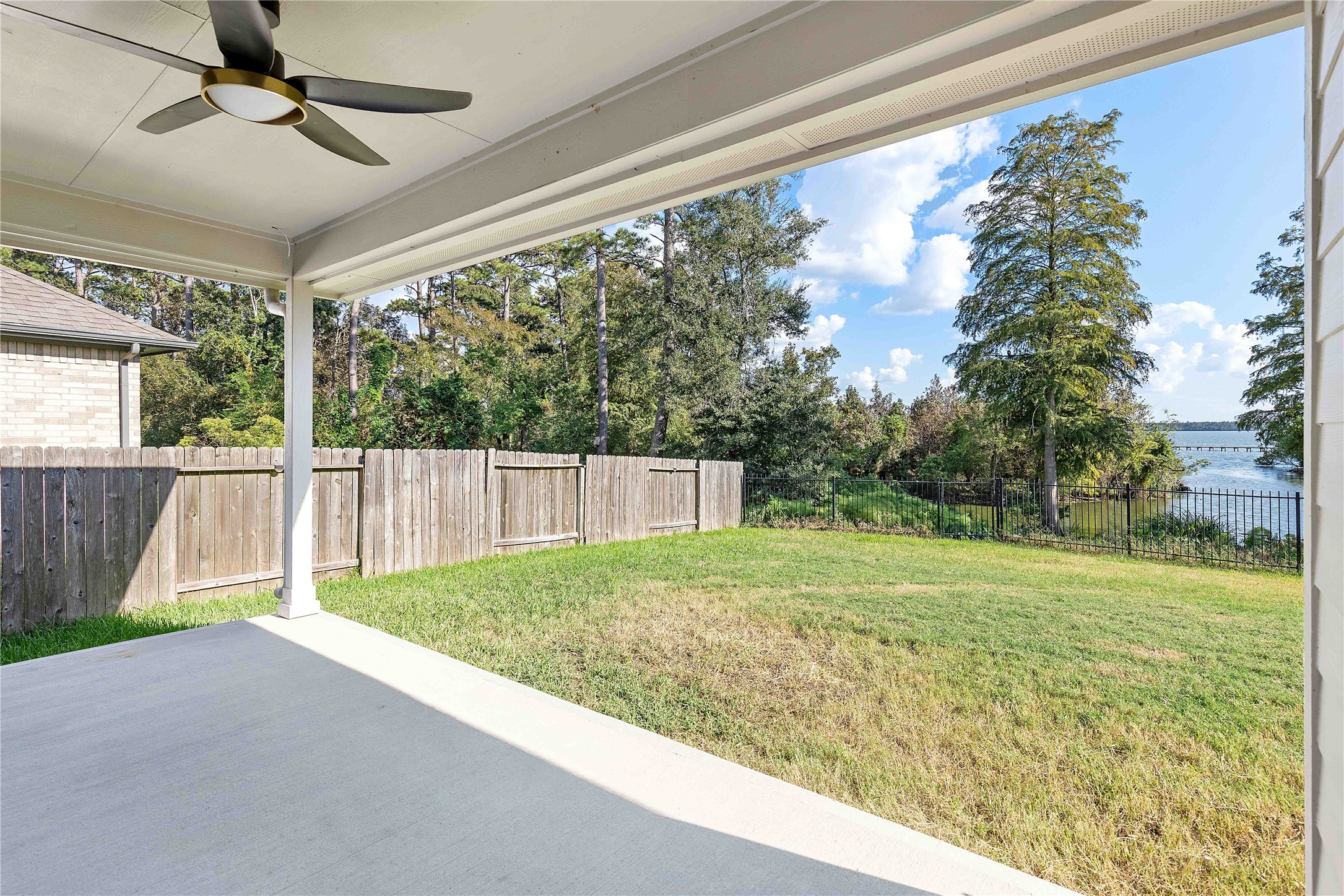 Spacious covered patio with a ceiling fan overlooking a lush backyard and serene water views, perfect for outdoor relaxation and entertaining.