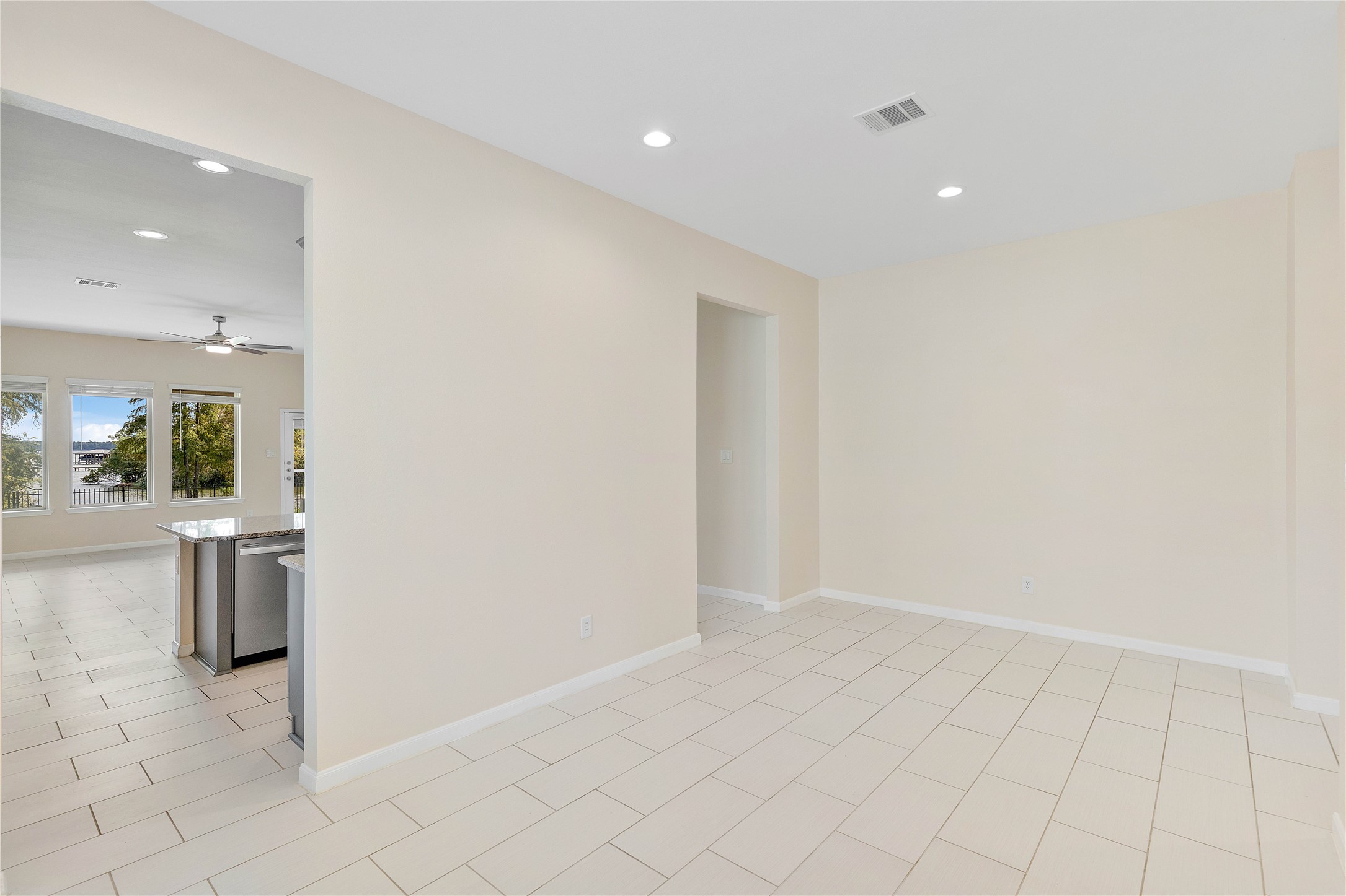 Spacious open concept & modern living area with sleek tile flooring, neutral walls, and abundant natural light from large windows, seamlessly connected to a modern kitchen with stainless steel appliances and a ceiling fan.
