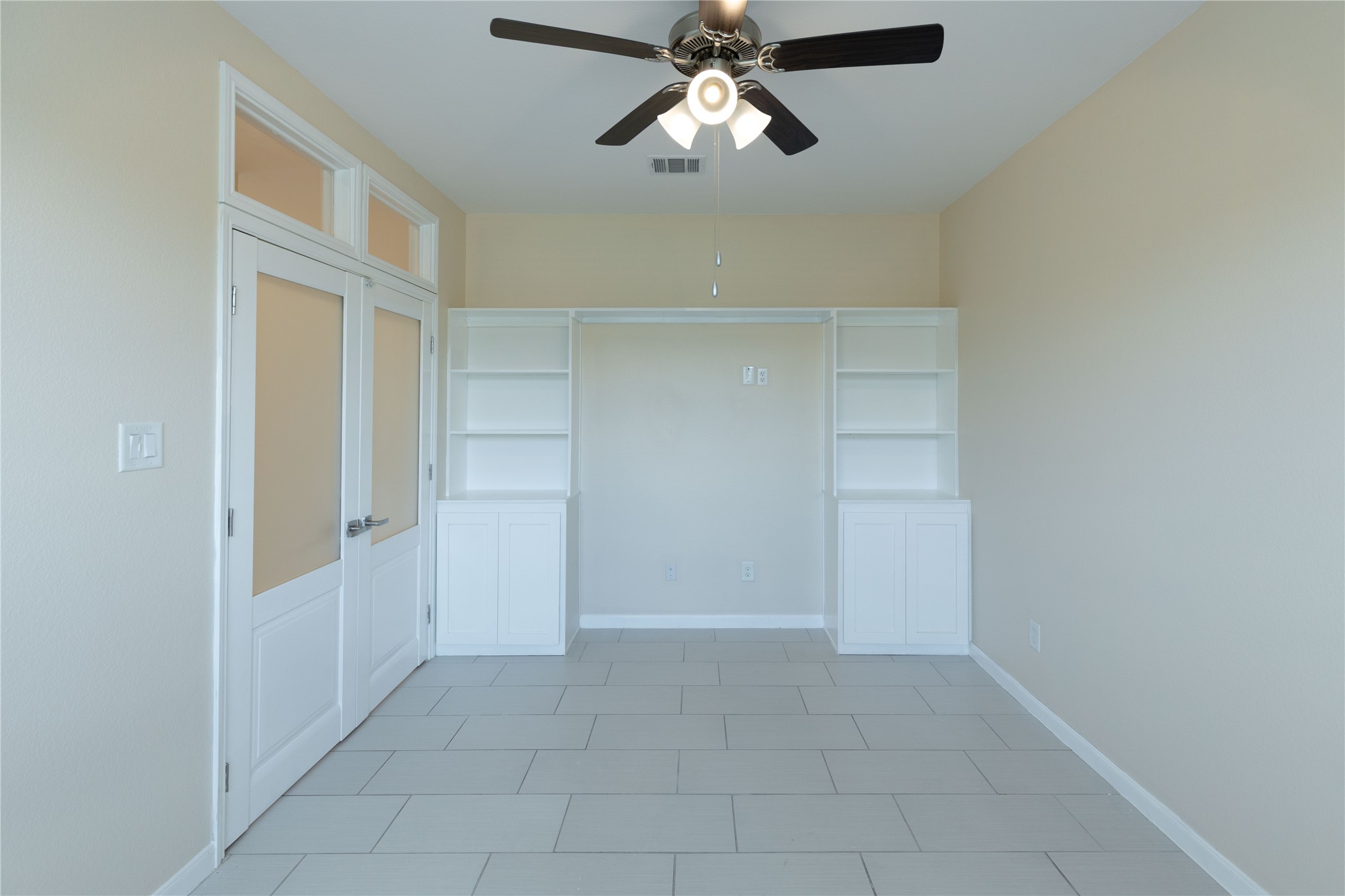 Bright and inviting, this home office/guest bedroom features elegant French doors, built-in shelving, and a ceiling fan, creating the perfect blend of style and functionality for your productive space.