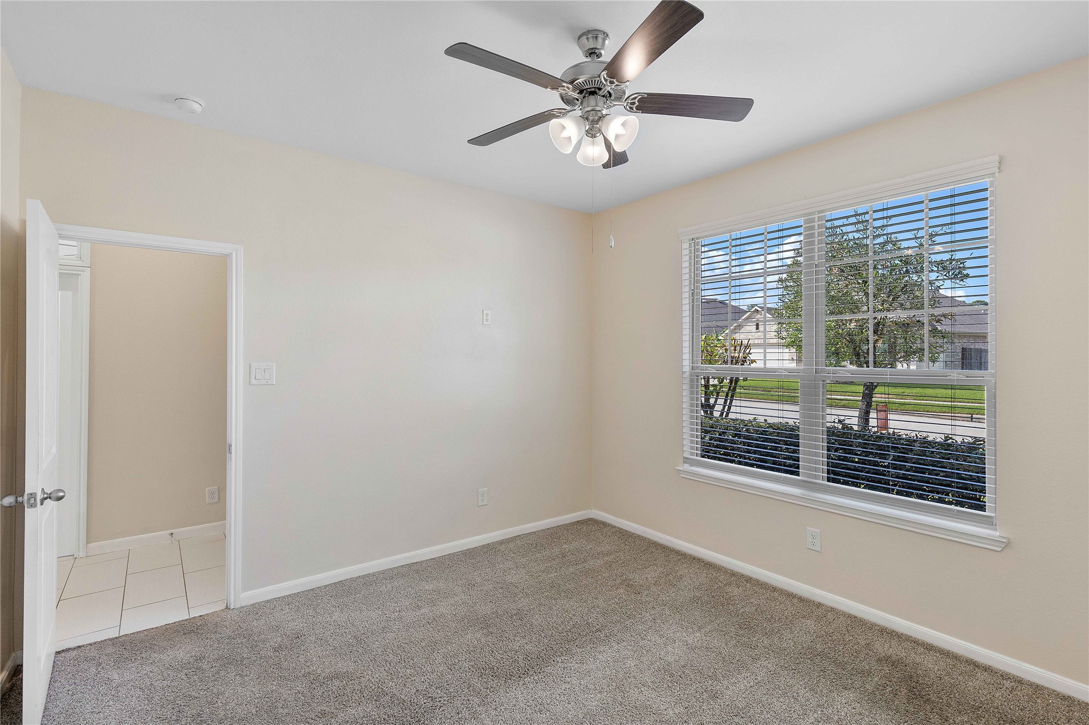 Bright and inviting room featuring plush carpeting, a ceiling fan, and a large window offering plenty of natural light.