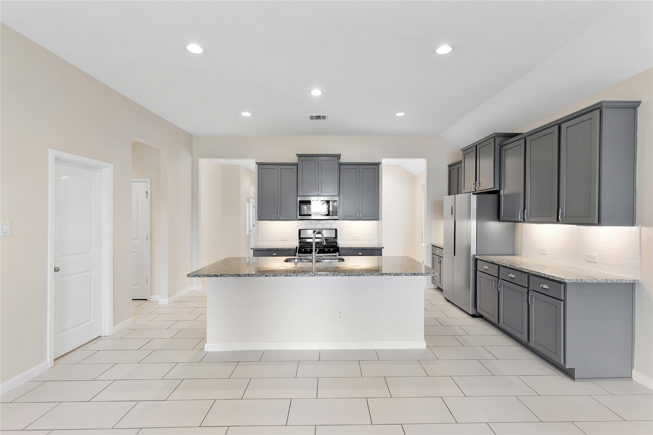 Modern kitchen with sleek gray cabinetry, granite countertops, and stainless steel appliances, offering ample space and contemporary style.