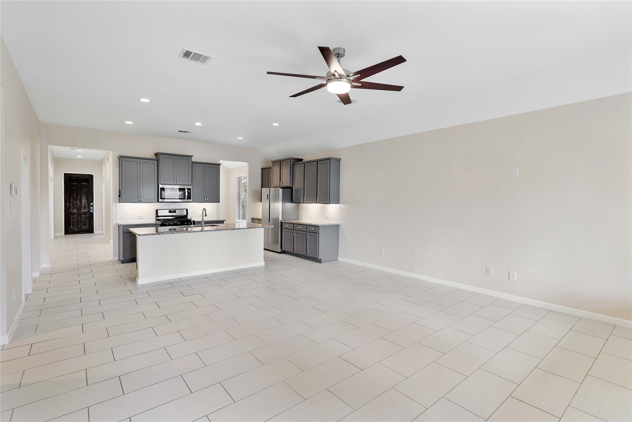 Spacious open-concept living area with sleek tile flooring and a modern kitchen featuring stainless steel appliances and gray cabinetry, perfect for entertaining and family gatherings.