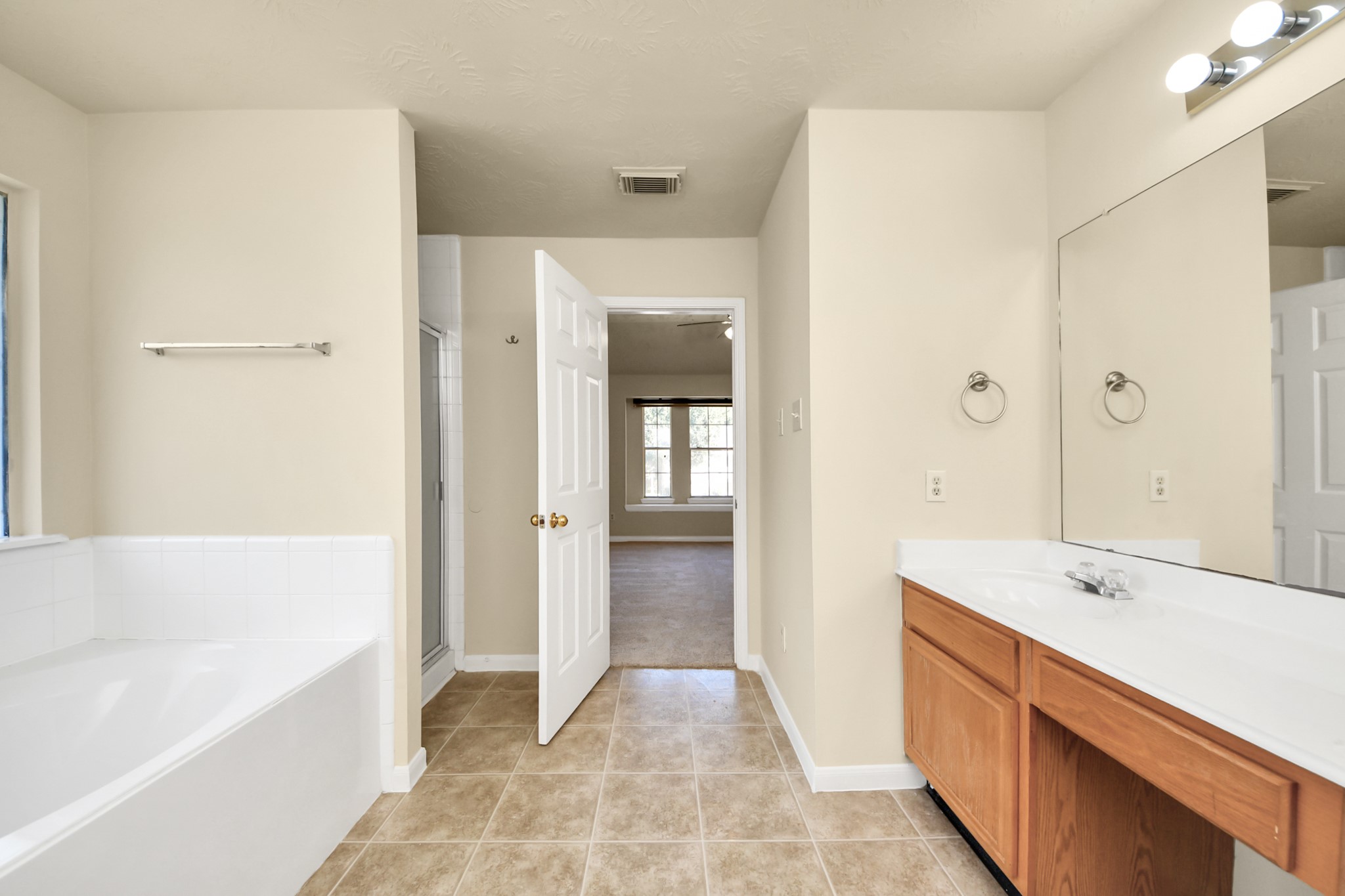 Spacious bathroom featuring a large soaking tub, dual-sink vanity, tile flooring, and large closet.