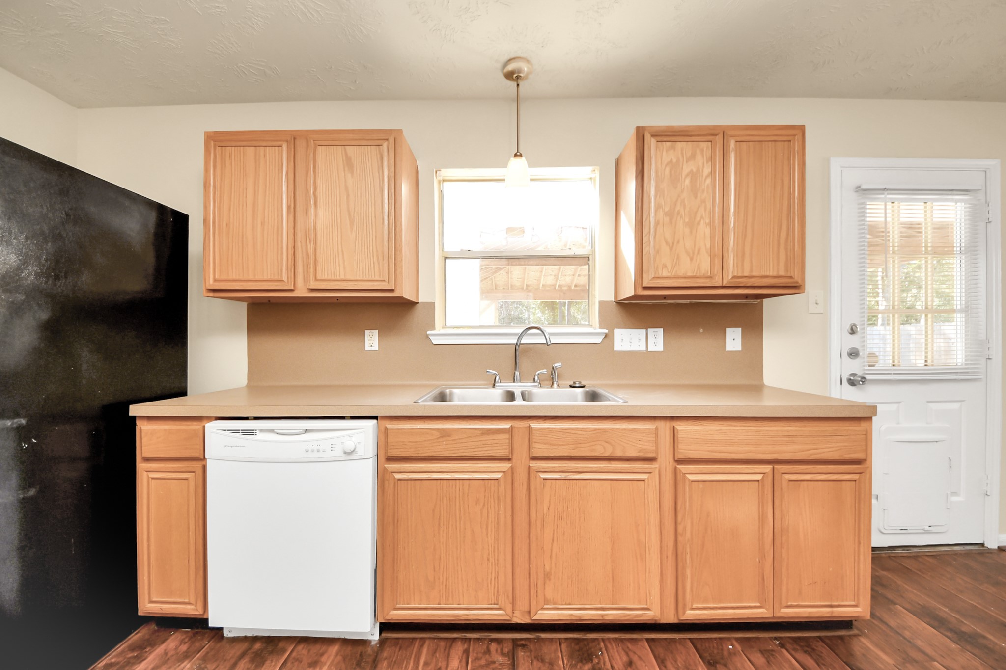 Bright kitchen with a double sink, appliances included, featuring a window and door leading to covered patio in your large backyard.