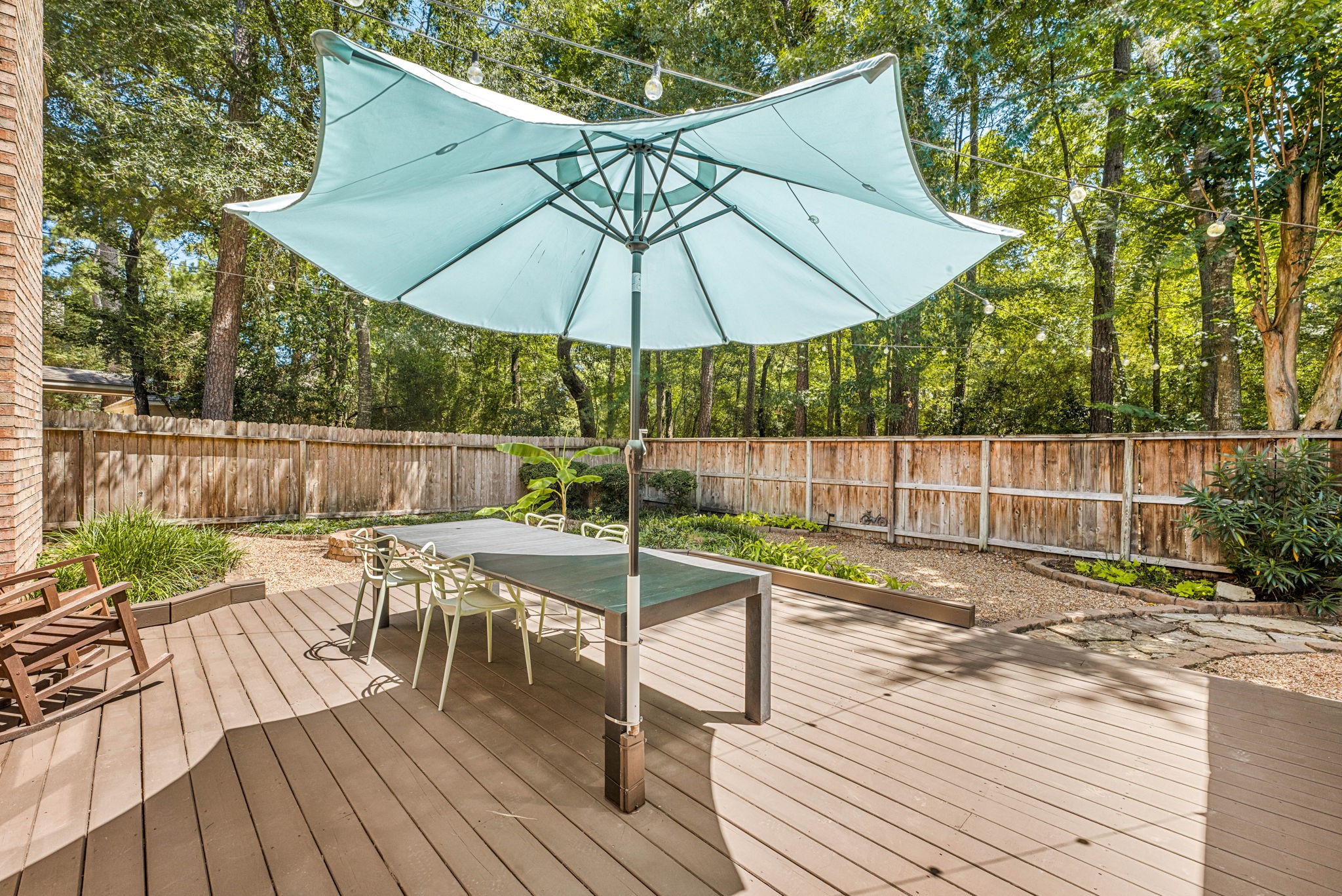 Spacious backyard deck  surrounded by lush greenery and a wooden fence, perfect for outdoor dining and relaxation.
