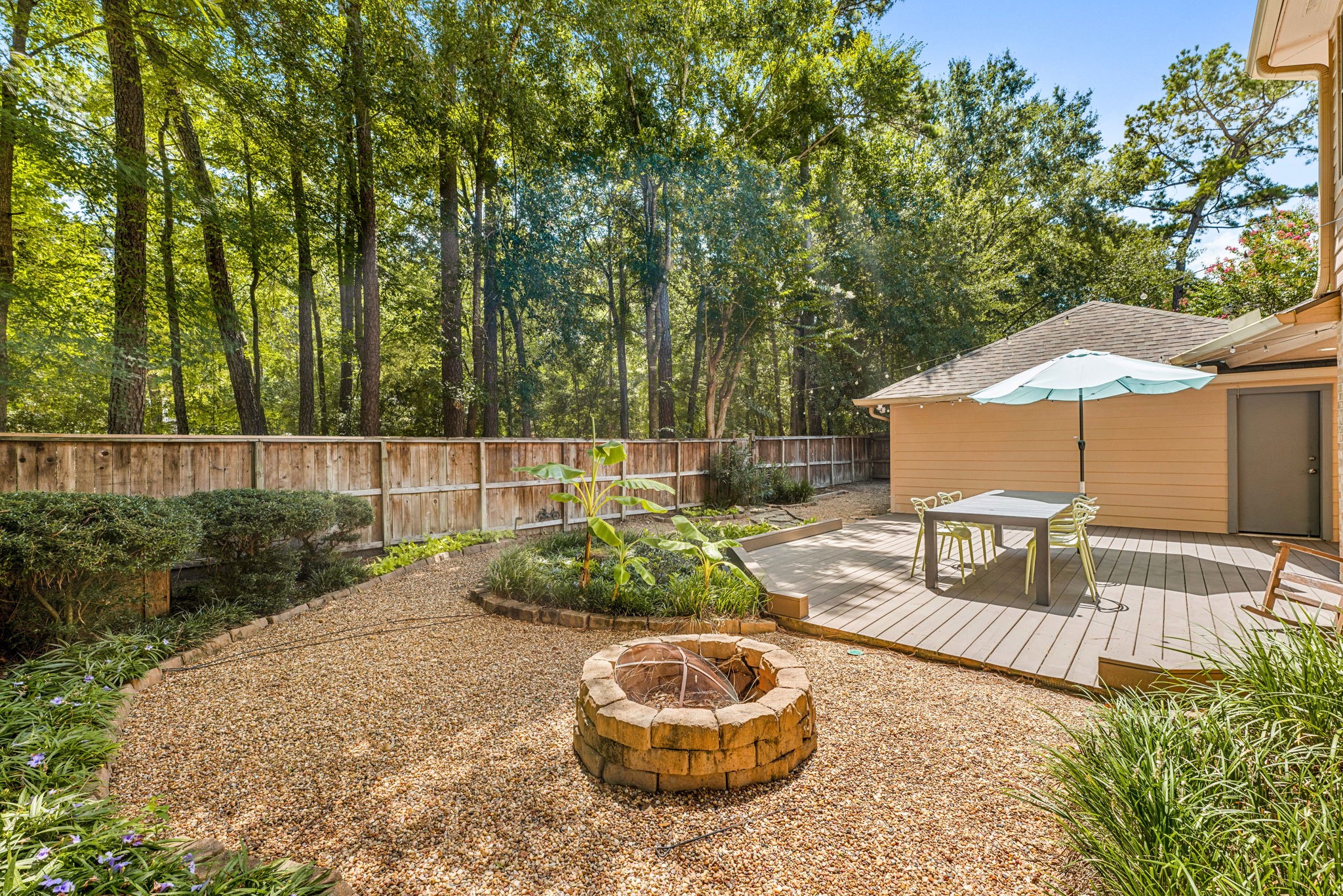 Charming backyard oasis with a spacious deck, shaded seating area, and a cozy fire pit, all set against a backdrop of lush, mature trees for privacy and tranquility.