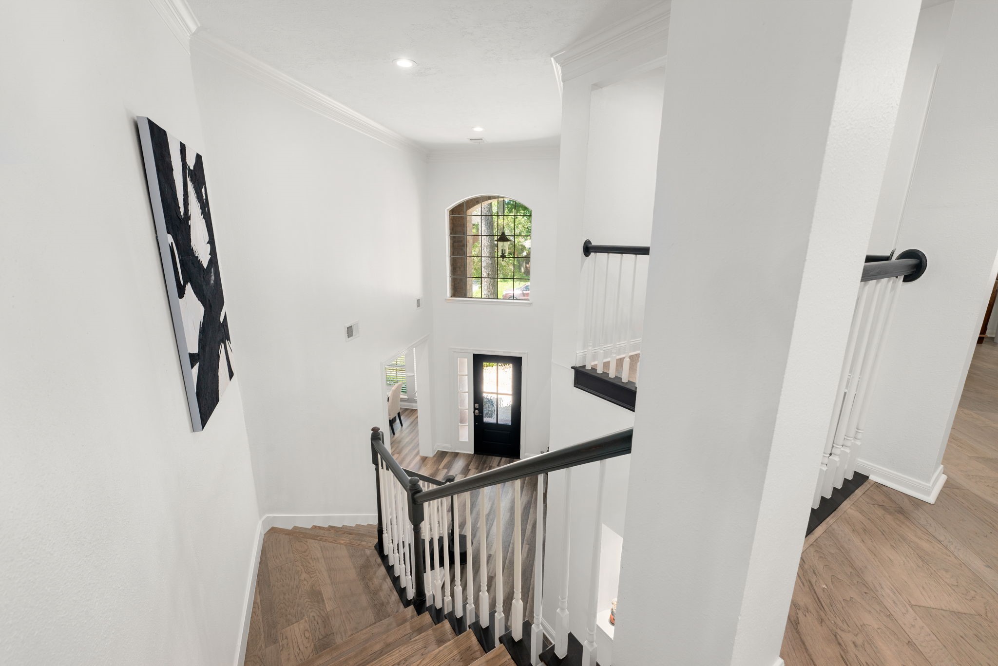 Elegant staircase with dark wood railing and white spindles leads to a bright entryway, featuring a large arched window that fills the space with natural light.