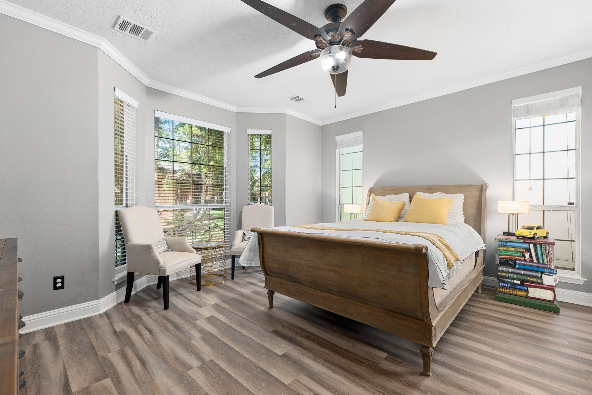 Bright and inviting primary bedroom featuring large bay windows, elegant wood floors, and a stylish ceiling fan, creating a cozy yet sophisticated atmosphere.