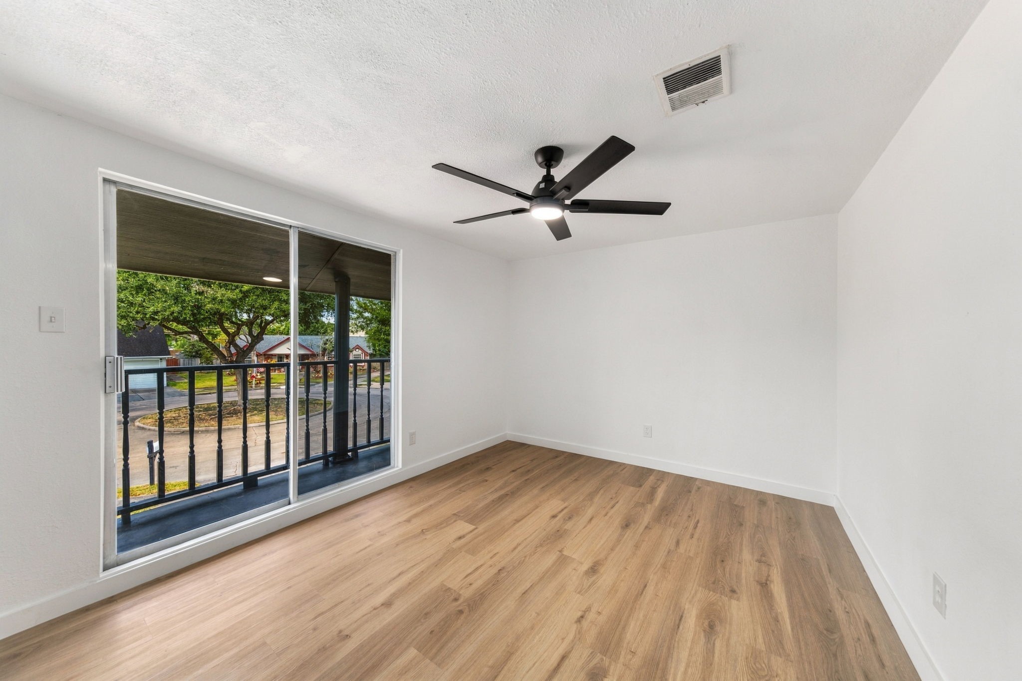 Light-filled secondary bedroom with fresh, neutral finishes and access to the front balcony through sliding glass doors.