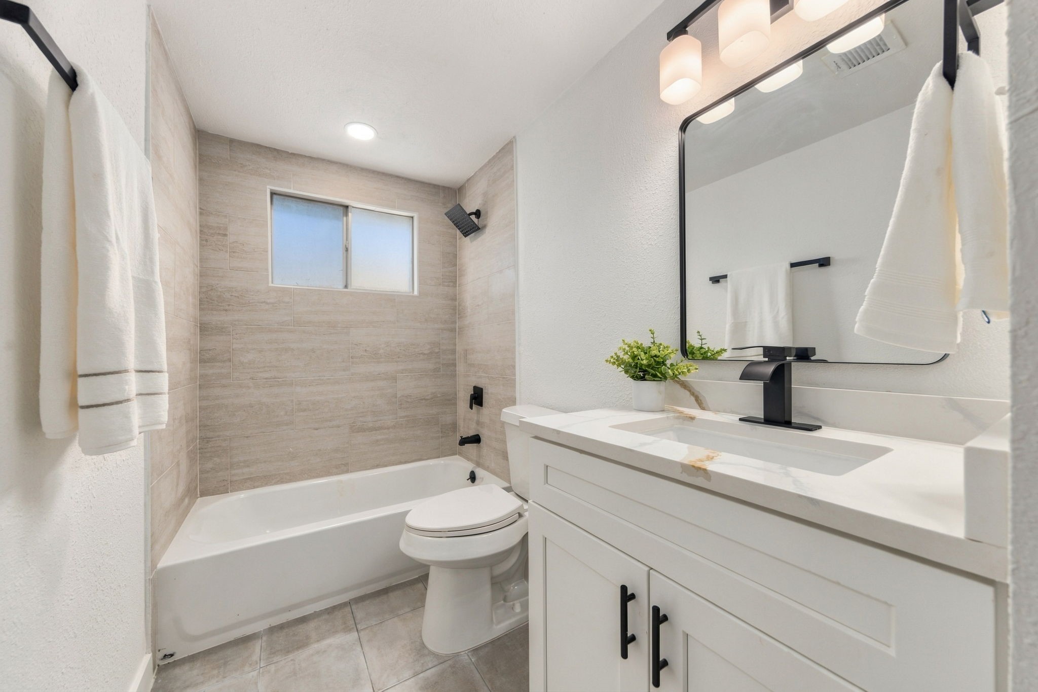 Updated upstairs bathroom with new tile surround, cabinetry, quartz countertops, fixtures, and lighting.