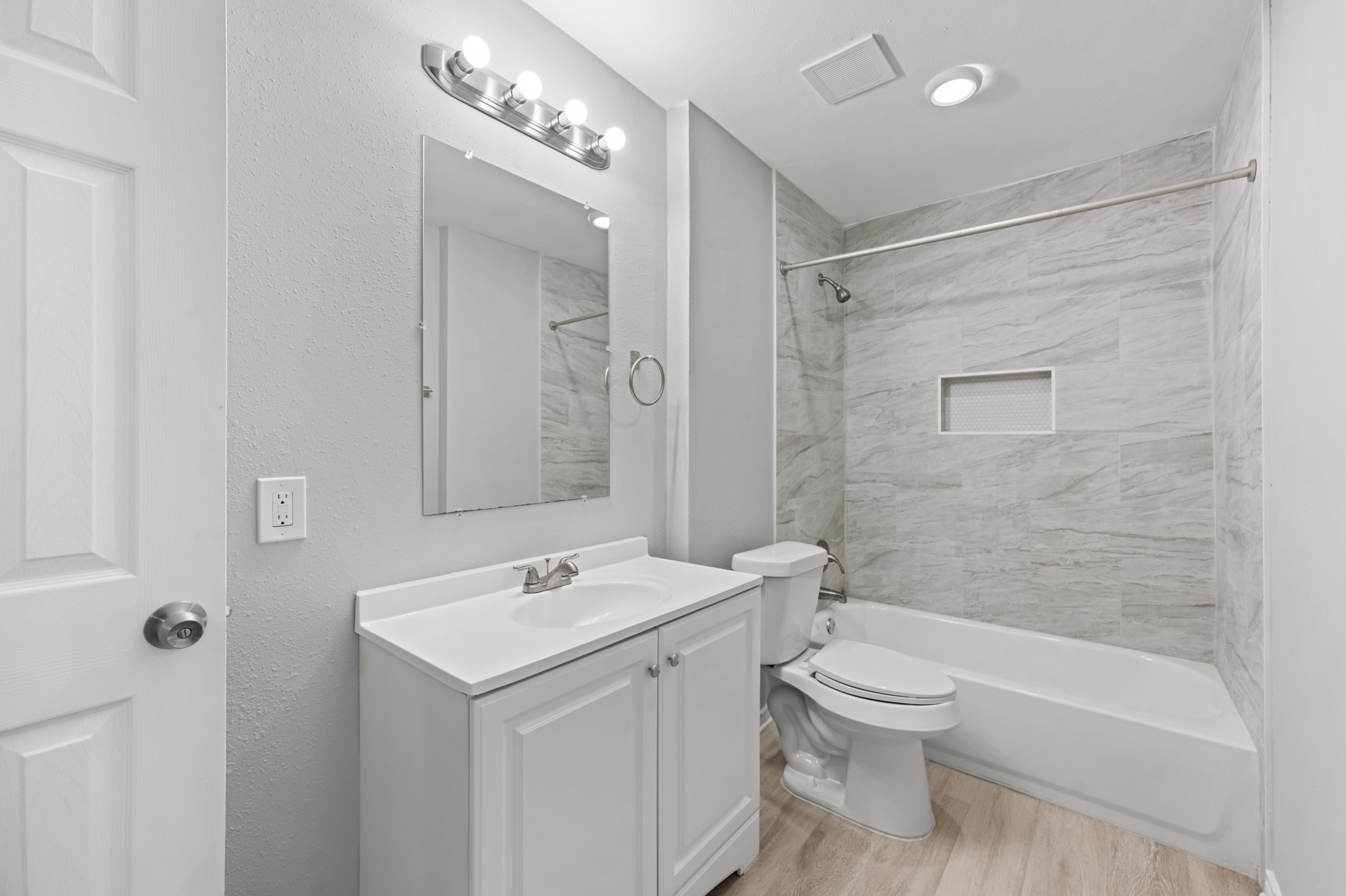 The updated guest bathroom features a white vanity, modern lighting, and a tub/shower combination with beautiful marble-look tile surround and a convenient recessed shower niche.
