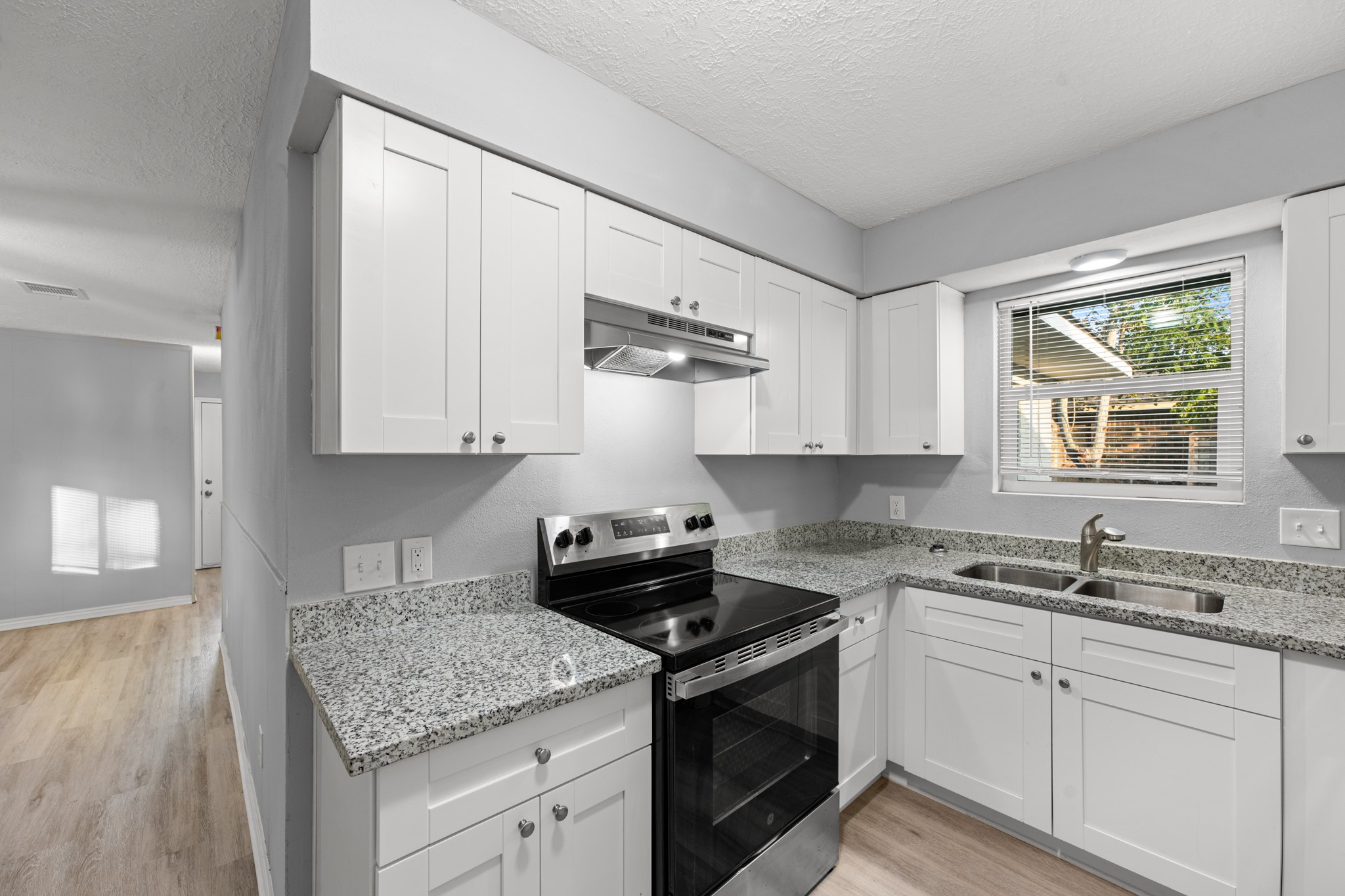 This inviting kitchen combines white shaker-style cabinetry, granite countertops, a stainless steel electric range, and a double-basin sink beneath a window overlooking the backyard.