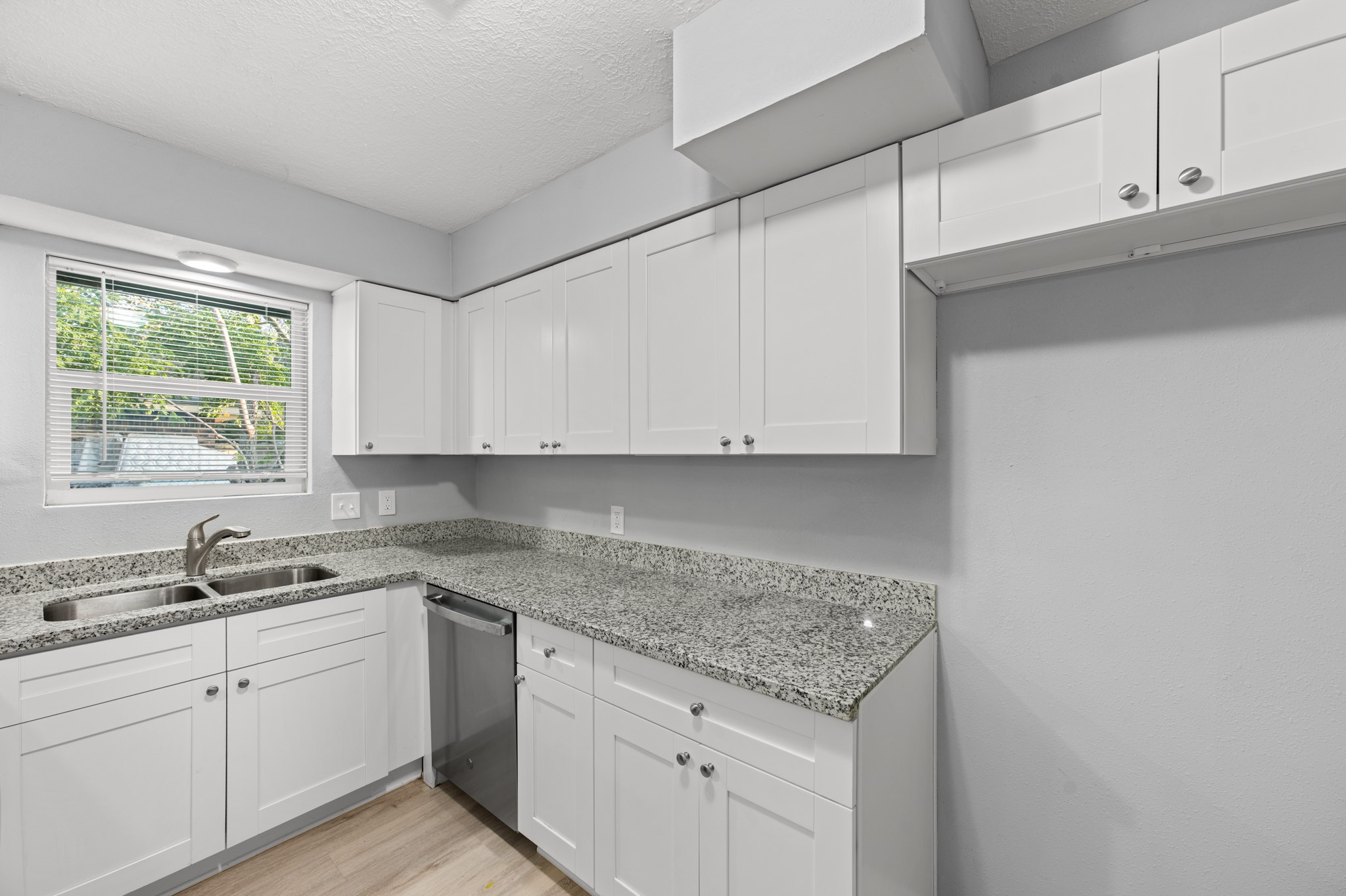 Expansive granite countertops provide plenty of room for meal preparation, complemented by white shaker-style cabinetry, a stainless steel dishwasher, and a double-basin sink overlooking the outdoors.
