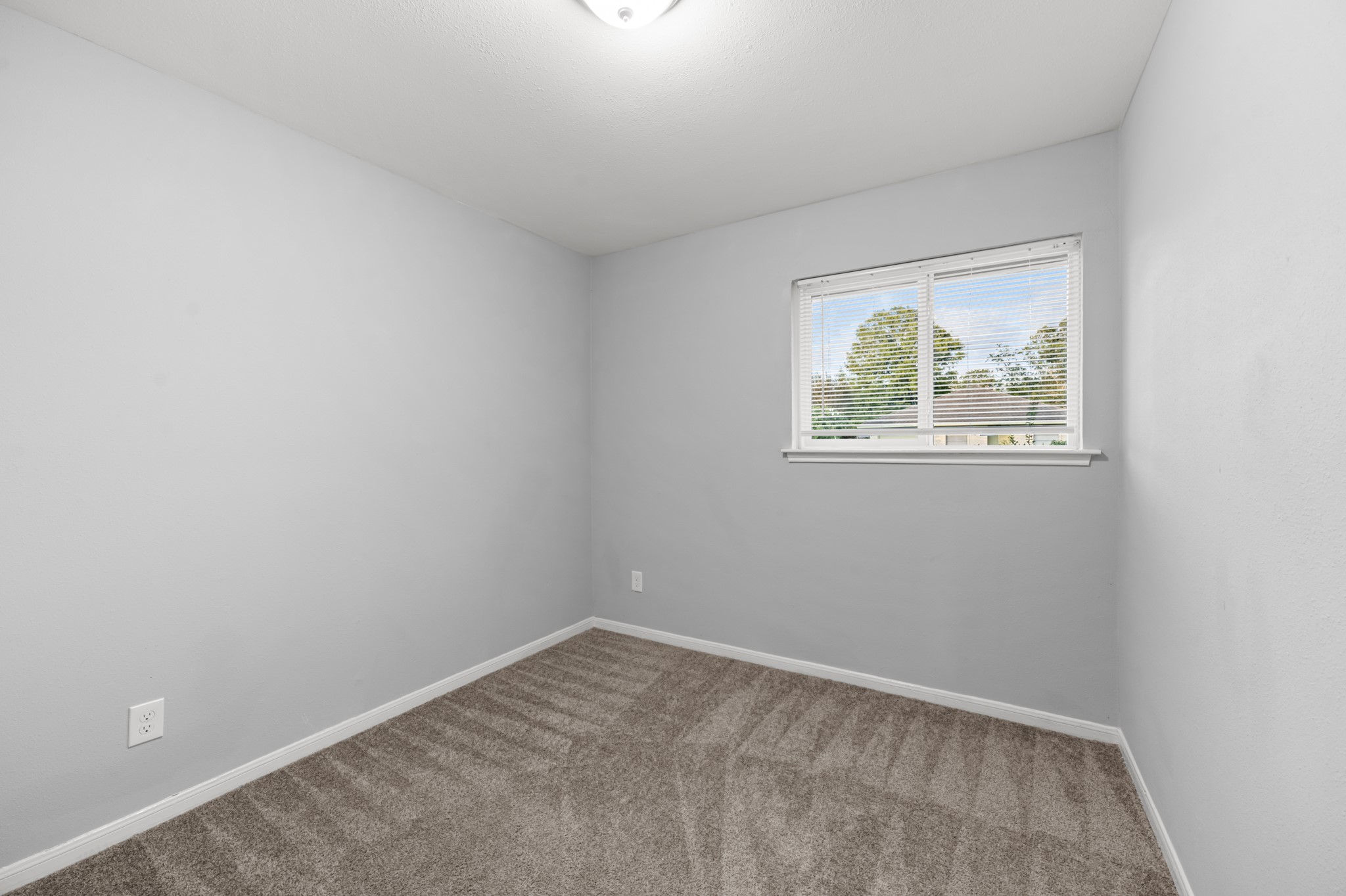 This inviting secondary bedroom features soft neutral wall colors, plush carpeting, and a window that welcomes natural light, creating a comfortable and versatile space.