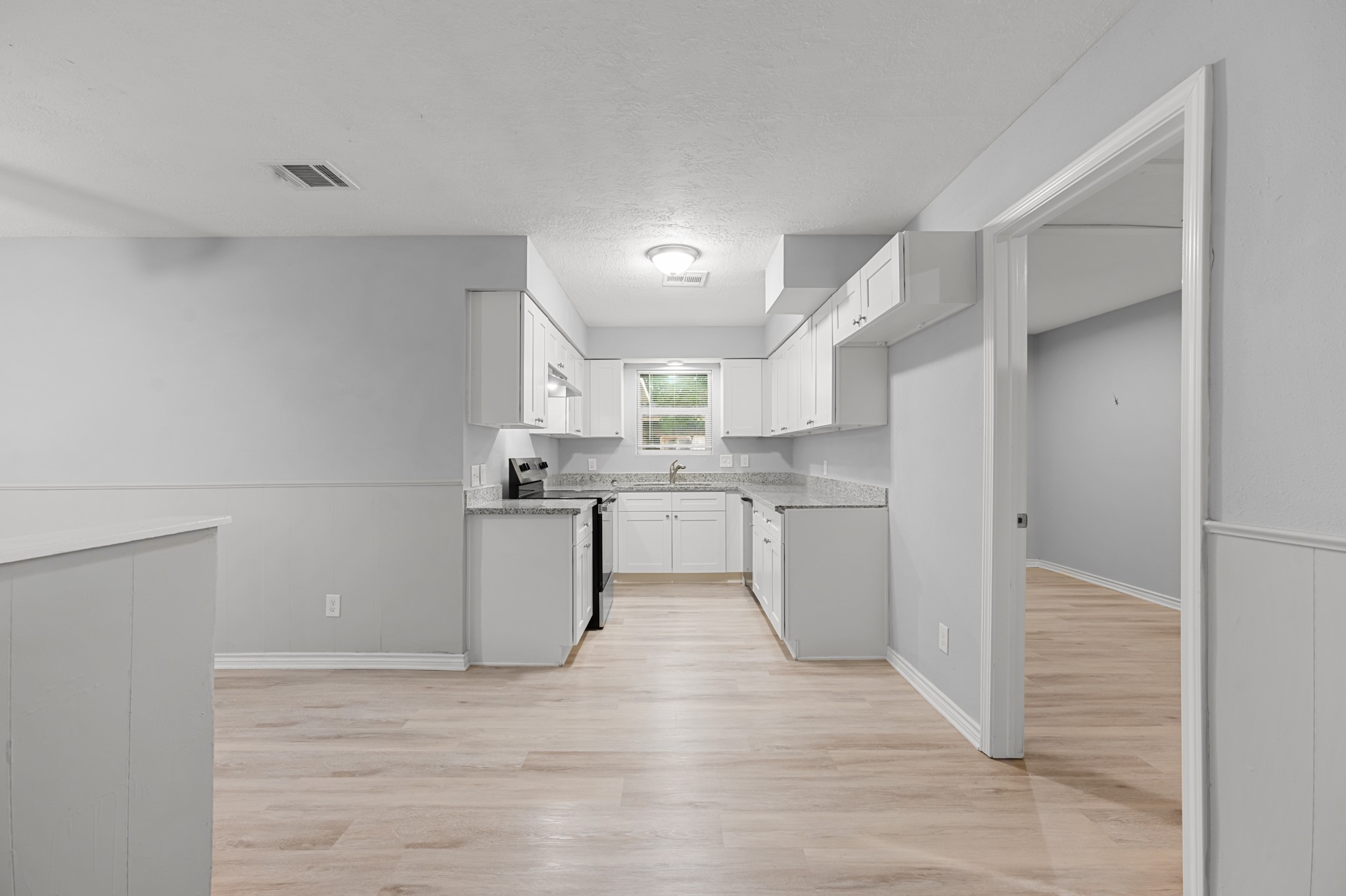 The updated galley-style kitchen features crisp white shaker-style cabinetry, granite countertops, stainless steel appliances, and wood-look flooring. Generous counter space and cabinetry provide functionality for everyday cooking and entertaining.