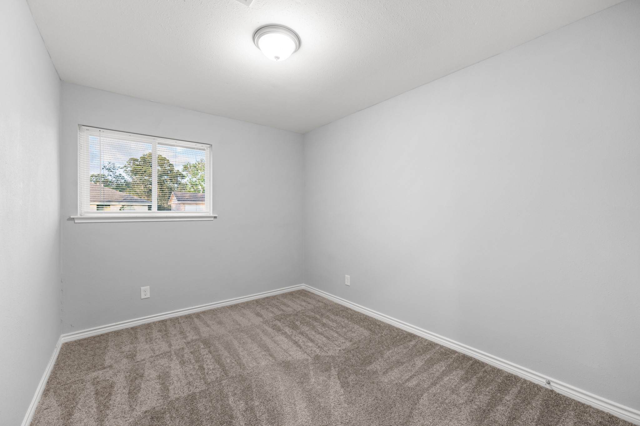 Another bedroom highlights the clean, neutral finishes, generous wall space for furniture placement, and natural light from the window.
