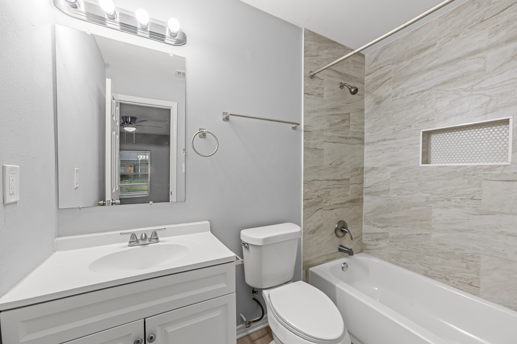 The private primary bathroom features a white vanity, tub and shower combination with marble-look tile surround, built-in shower niche, and brushed nickel fixtures for a fresh, modern appearance.