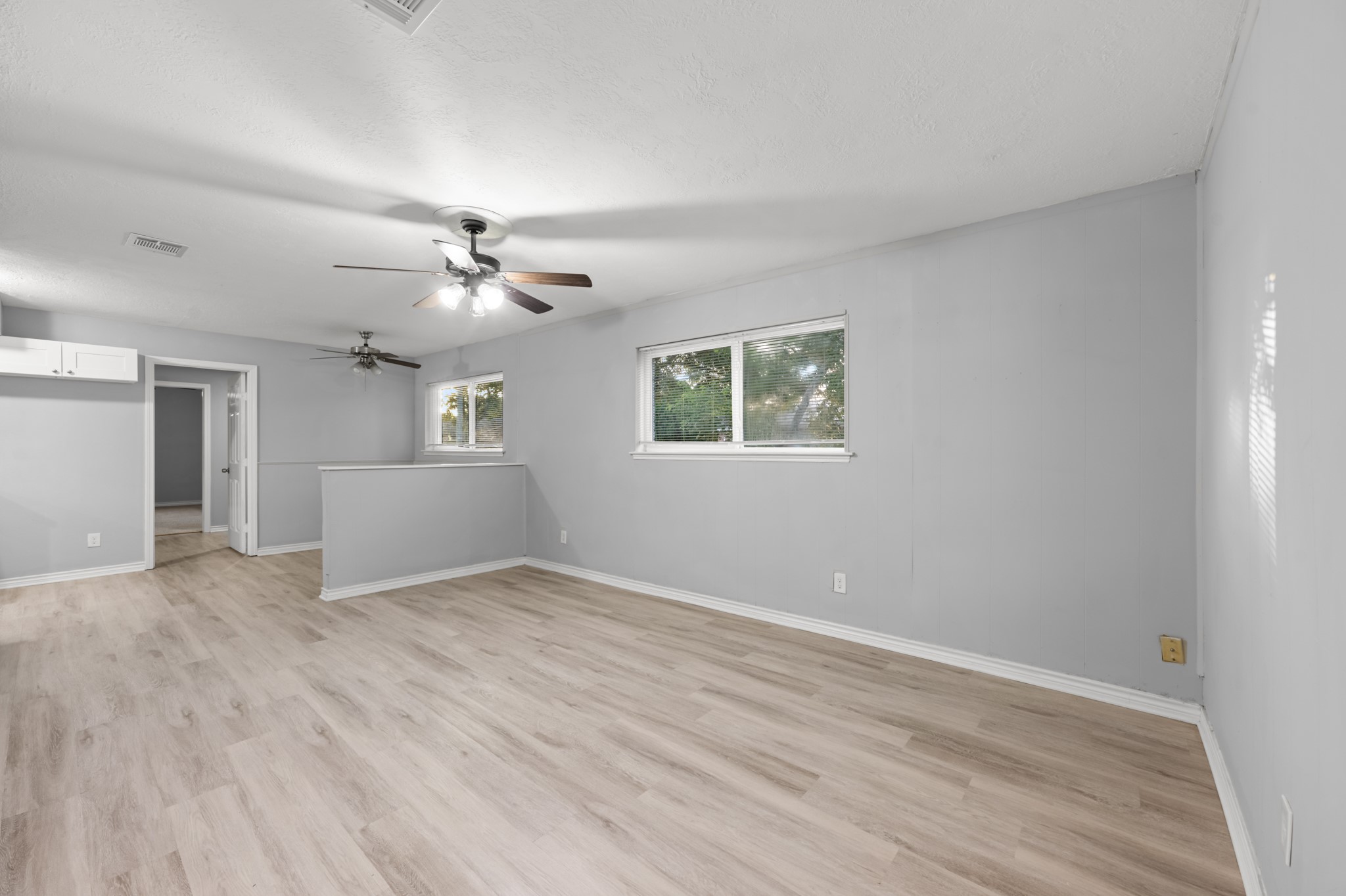 The spacious living room offers an inviting setting with wood-look flooring, neutral finishes, ceiling fan, and large windows that fill the space with natural light.