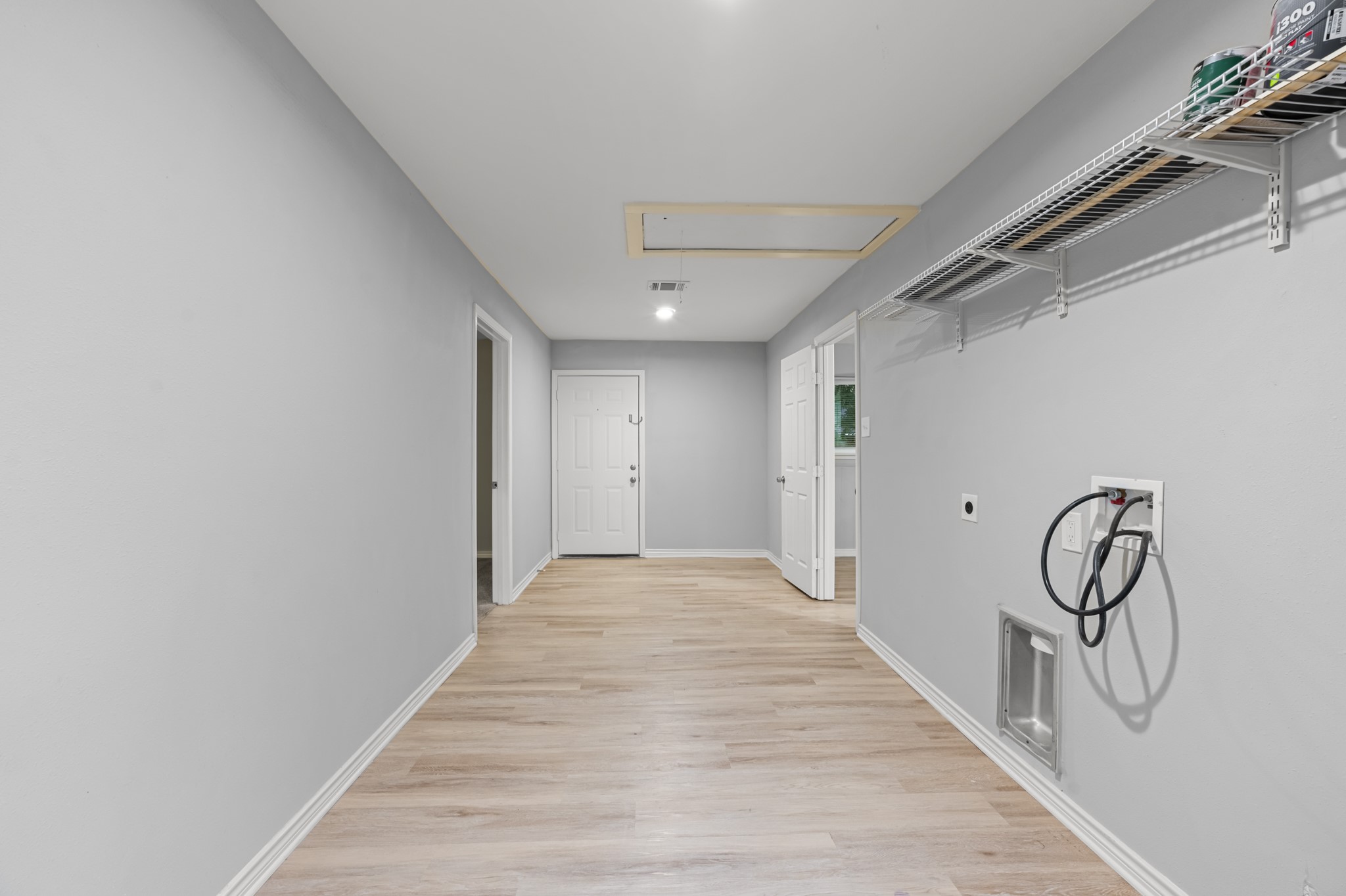 Another view of the utility room highlights the generous floor space, laundry hookups, and wall-mounted shelving, offering flexibility for laundry and household storage.