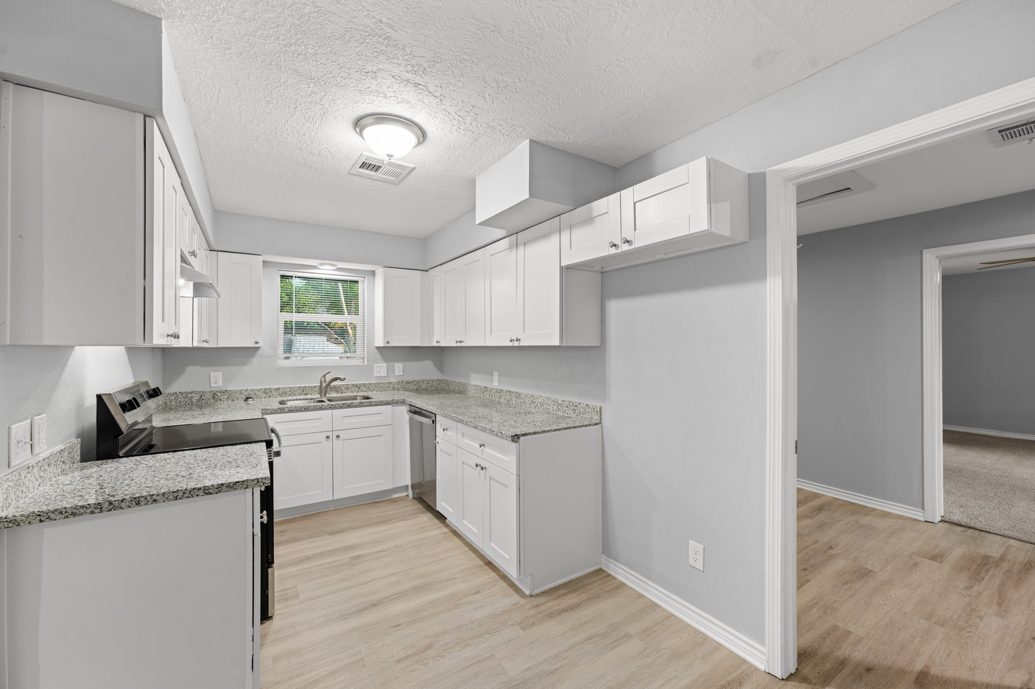 Another view of the updated kitchen highlights the wraparound granite countertops, stainless steel appliances, and convenient access to the adjoining rooms.