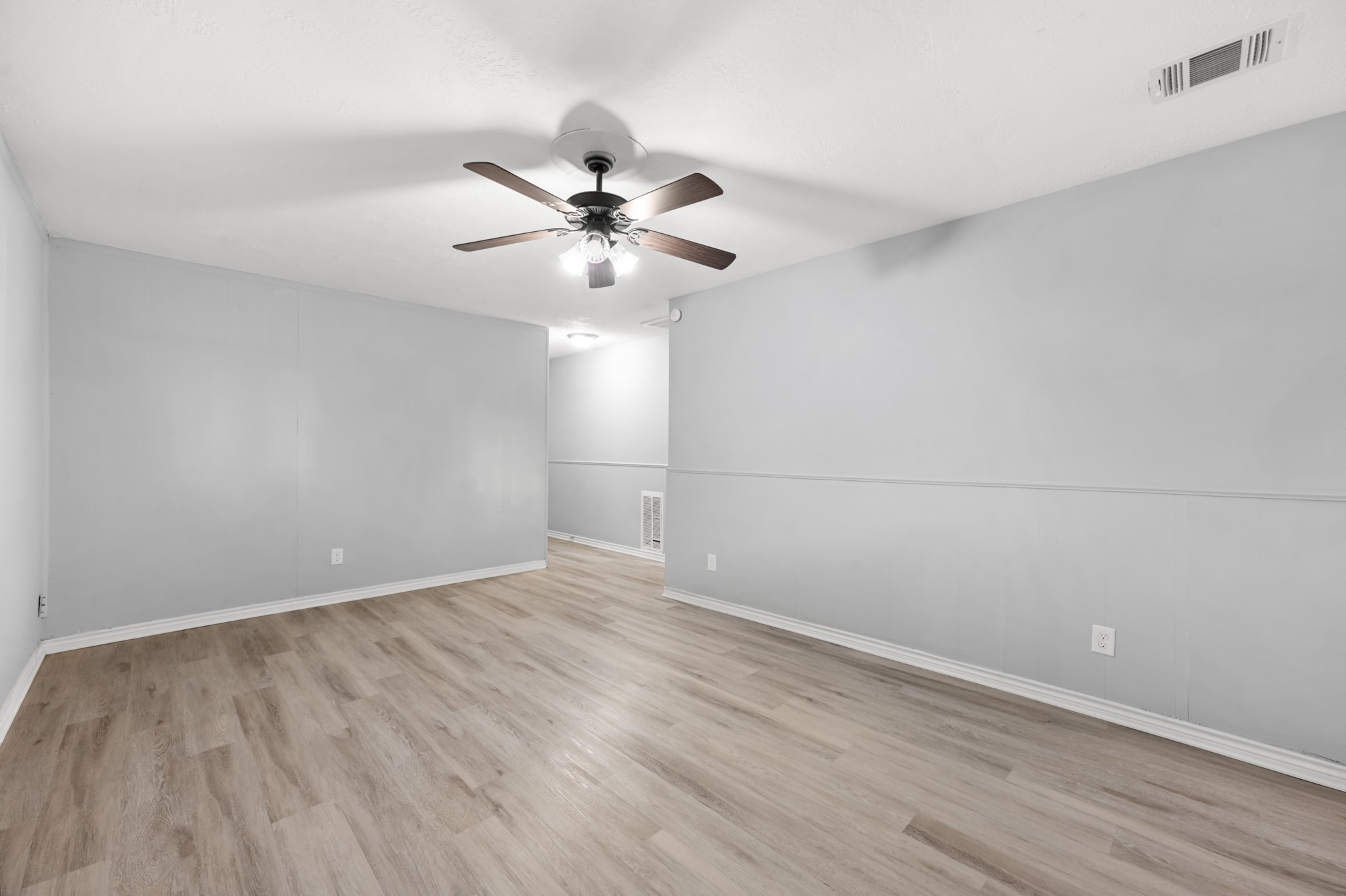 This generously sized living area features ample wall space for furniture arrangements, attractive wood-look flooring, and a ceiling fan with integrated lighting.