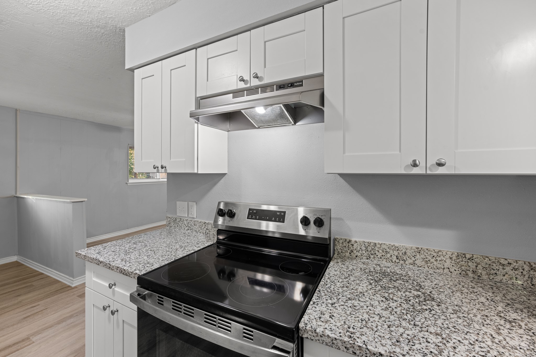 A closer look at the sleek electric range, stainless steel vent hood, granite countertops, and crisp white cabinetry that give this kitchen its fresh, modern appeal.