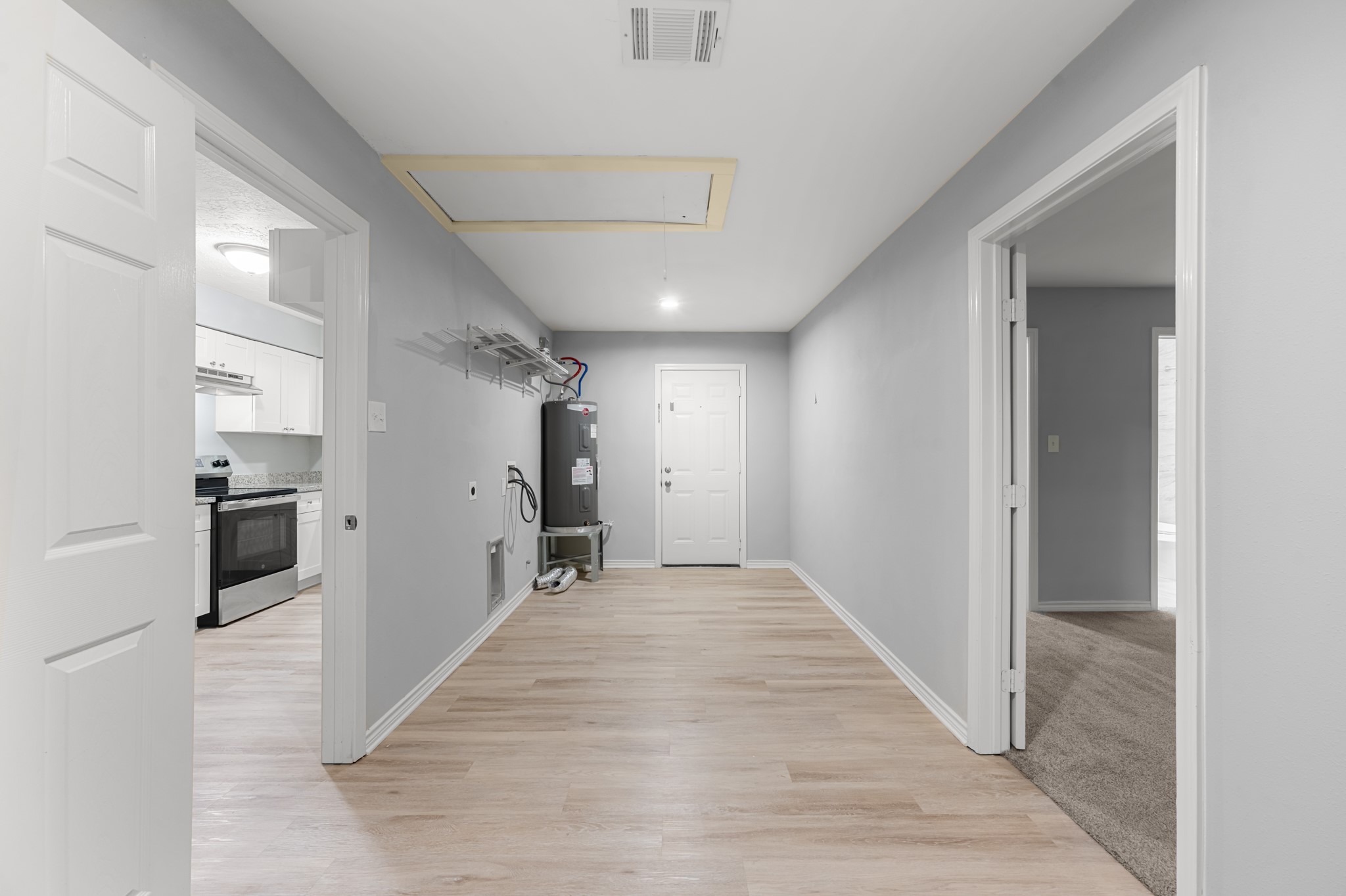 Spacious utility room with wood-look flooring, washer and dryer connections, overhead storage shelving, and convenient access to the kitchen and adjoining rooms.