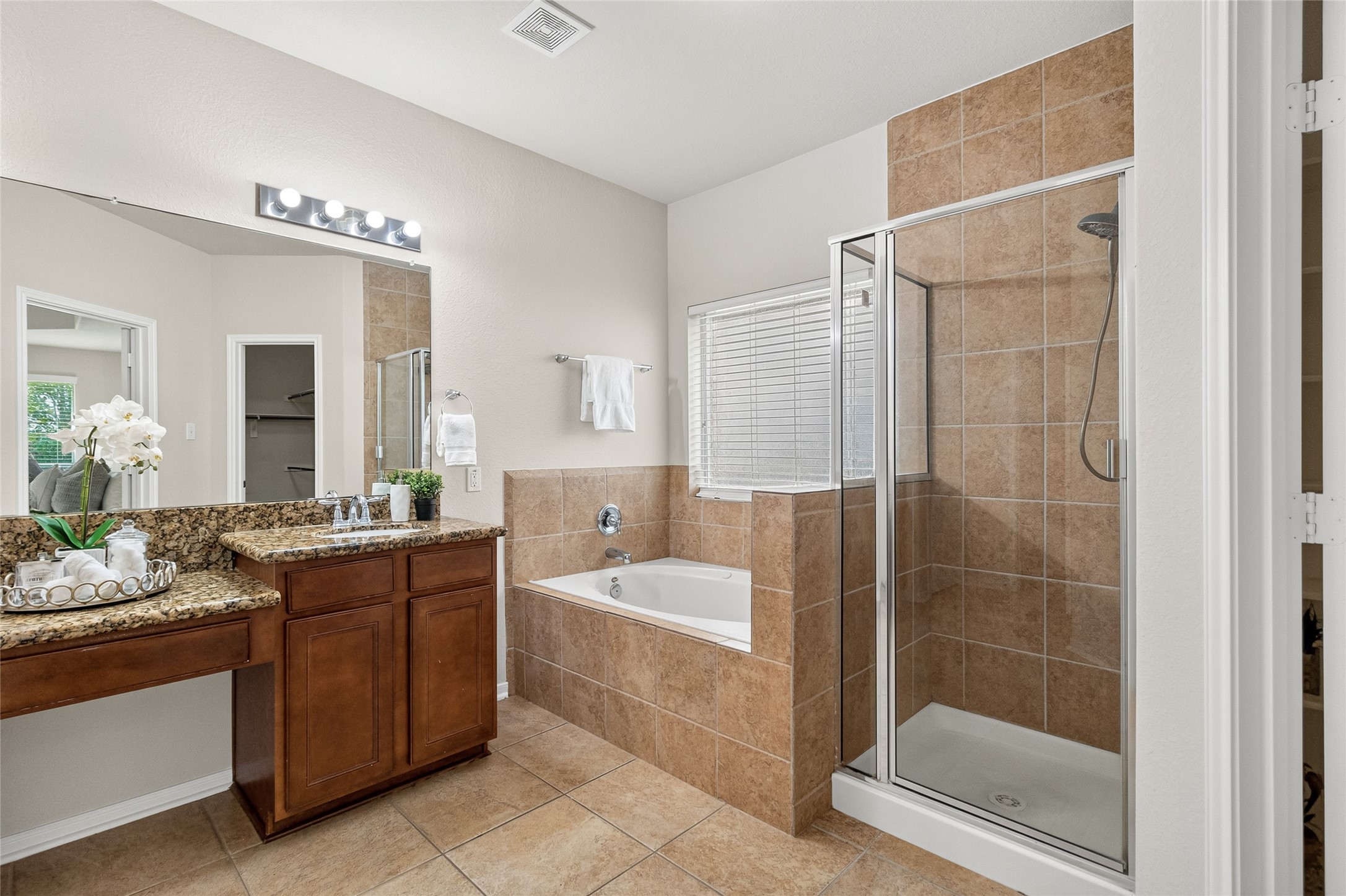 Your luxurious primary bath features a soaking tub, separate glass-enclosed shower, dual vanities, and direct access to the oversized walk-in closet.