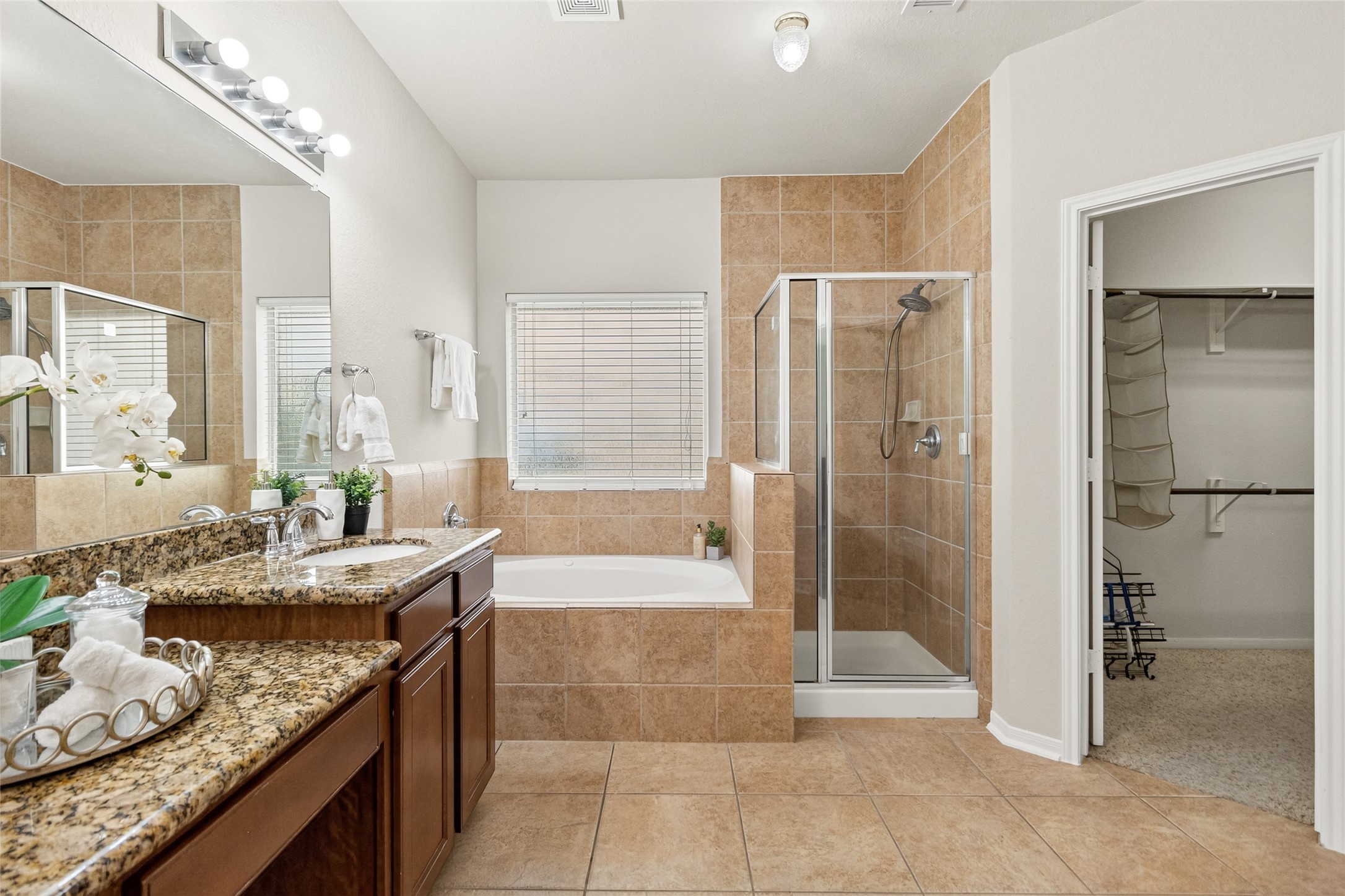 Your luxurious primary bath features a soaking tub, separate glass-enclosed shower, dual vanities, and direct access to the oversized walk-in closet.