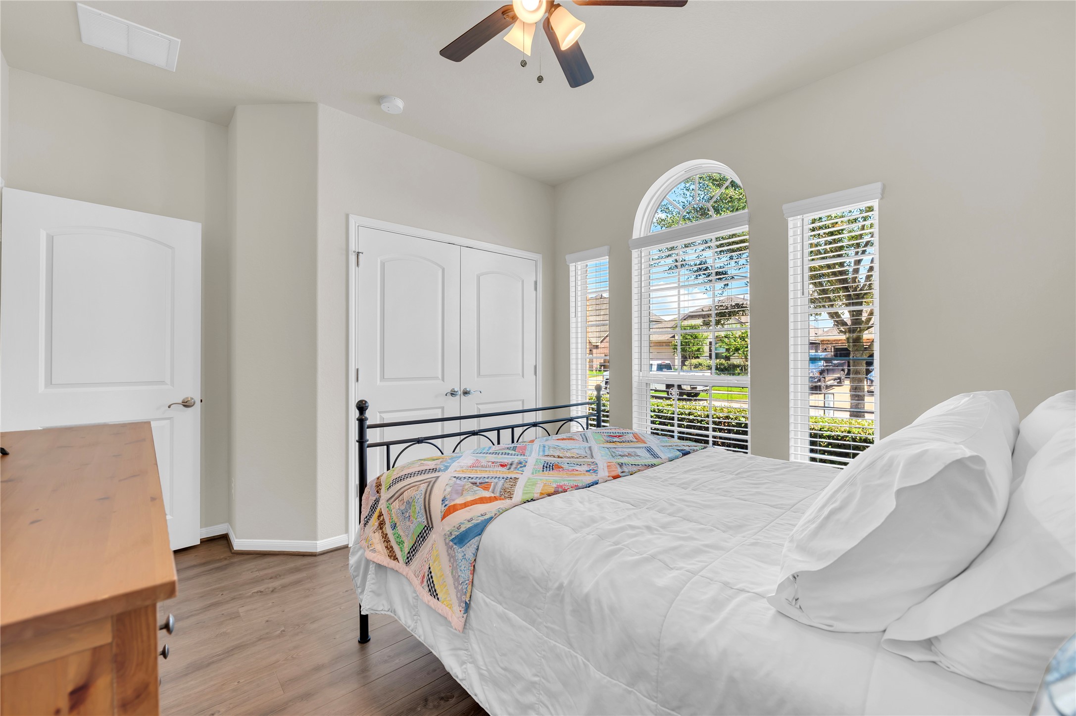 Bright and cozy bedroom featuring large arched windows that let in abundant natural light, complemented by elegant hardwood floors and a spacious closet.