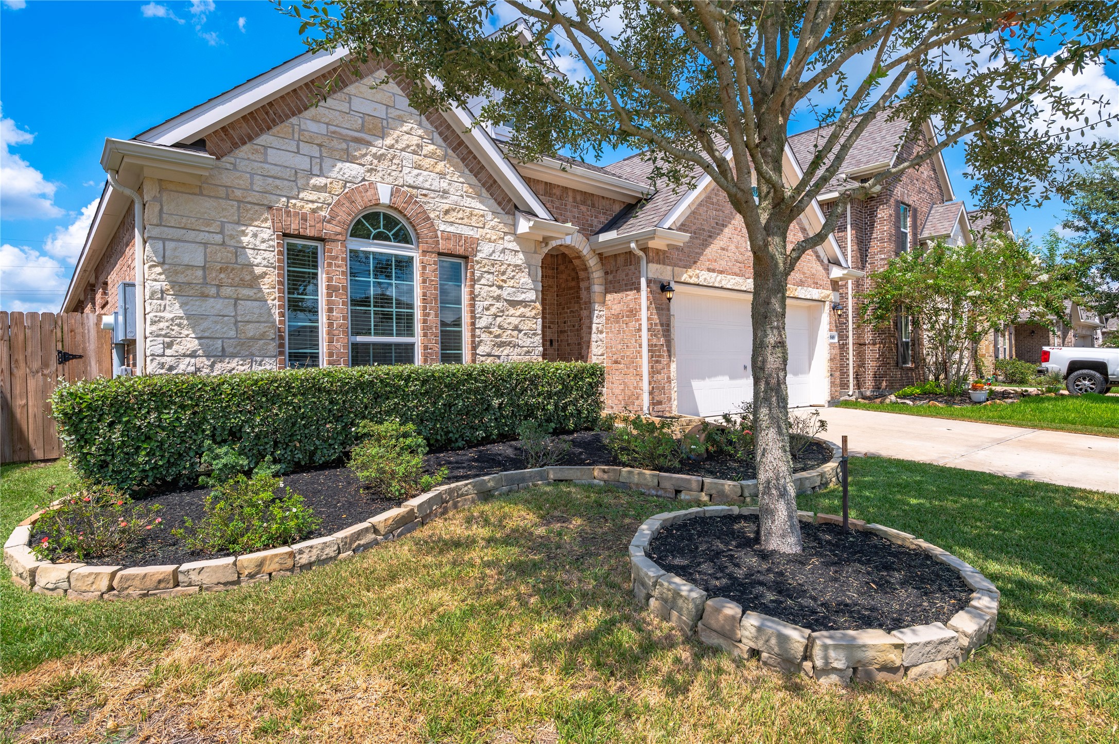 Charming brick and stone home with elegant arched windows, framed by manicured landscaping and a welcoming front yard tree.