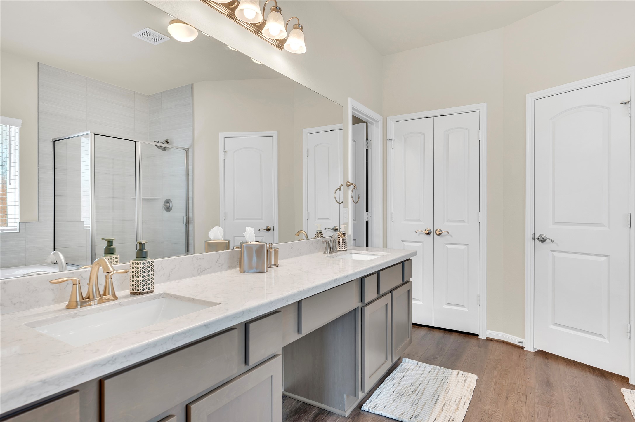 Elegant bathroom featuring a double vanity with marble countertops, modern fixtures, a glass-enclosed shower, and ample storage behind stylish cabinetry.