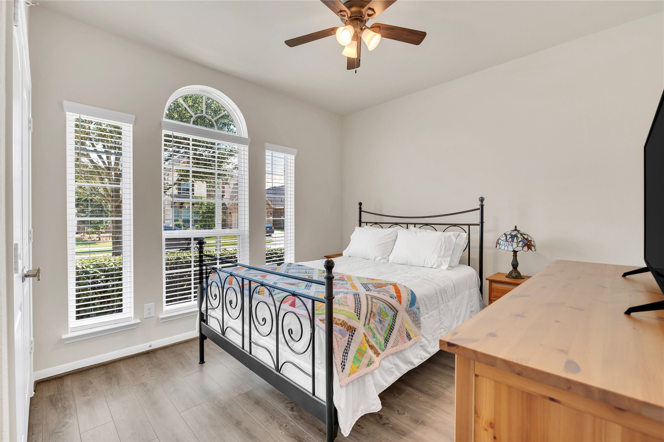 Charming bedroom with a natural light from large arched windows, complemented by a ceiling fan and elegant wood flooring.