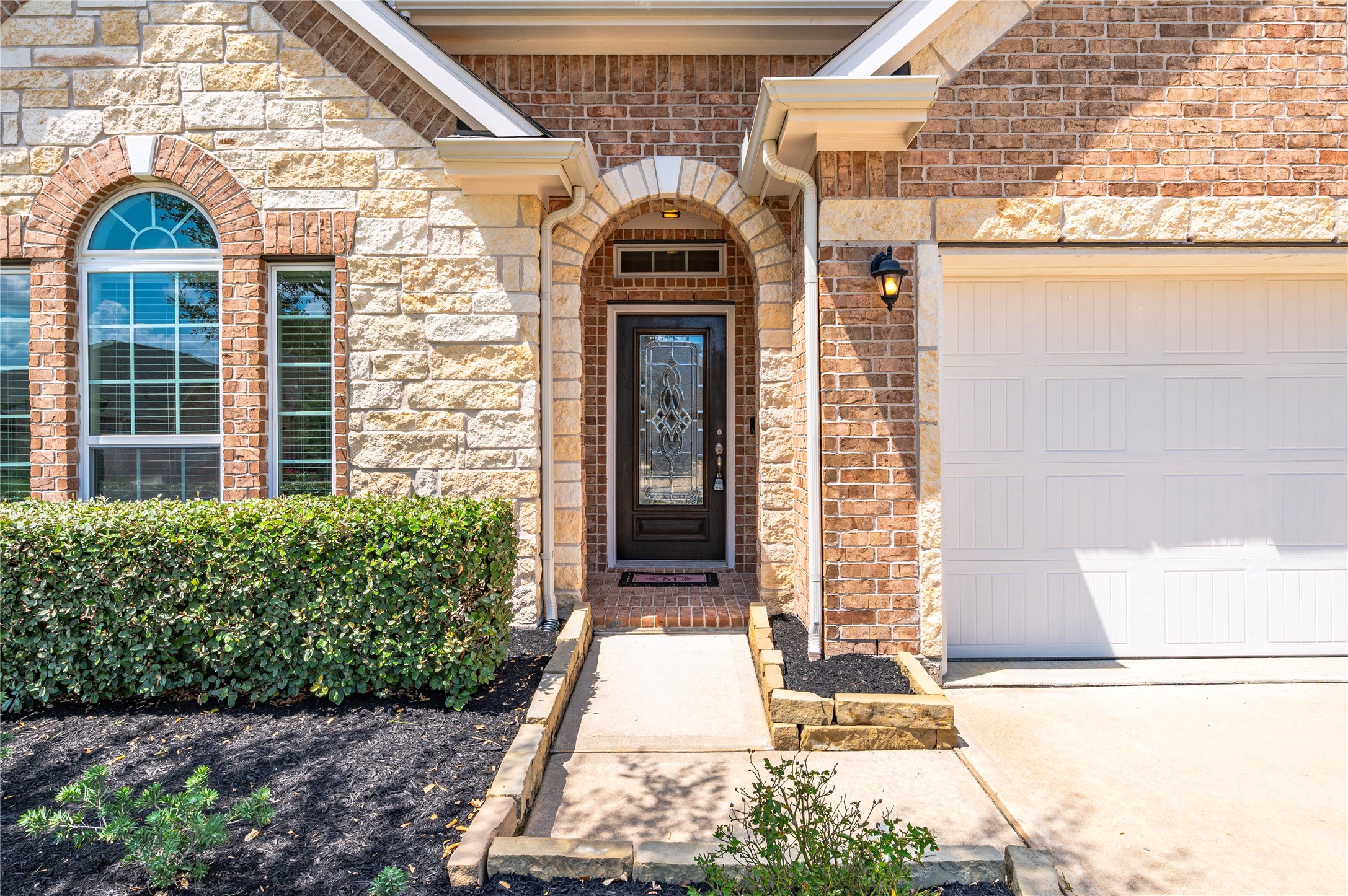 The welcoming entrance is a blend of stone and brick, featuring an archway and elegant glass front door, complemented by manicured landscaping and a cozy porch light. The welcoming entrance is a blend of stone and brick, featuring an archway and elegant glass front door, complemented by manicured landscaping and a cozy porch light.