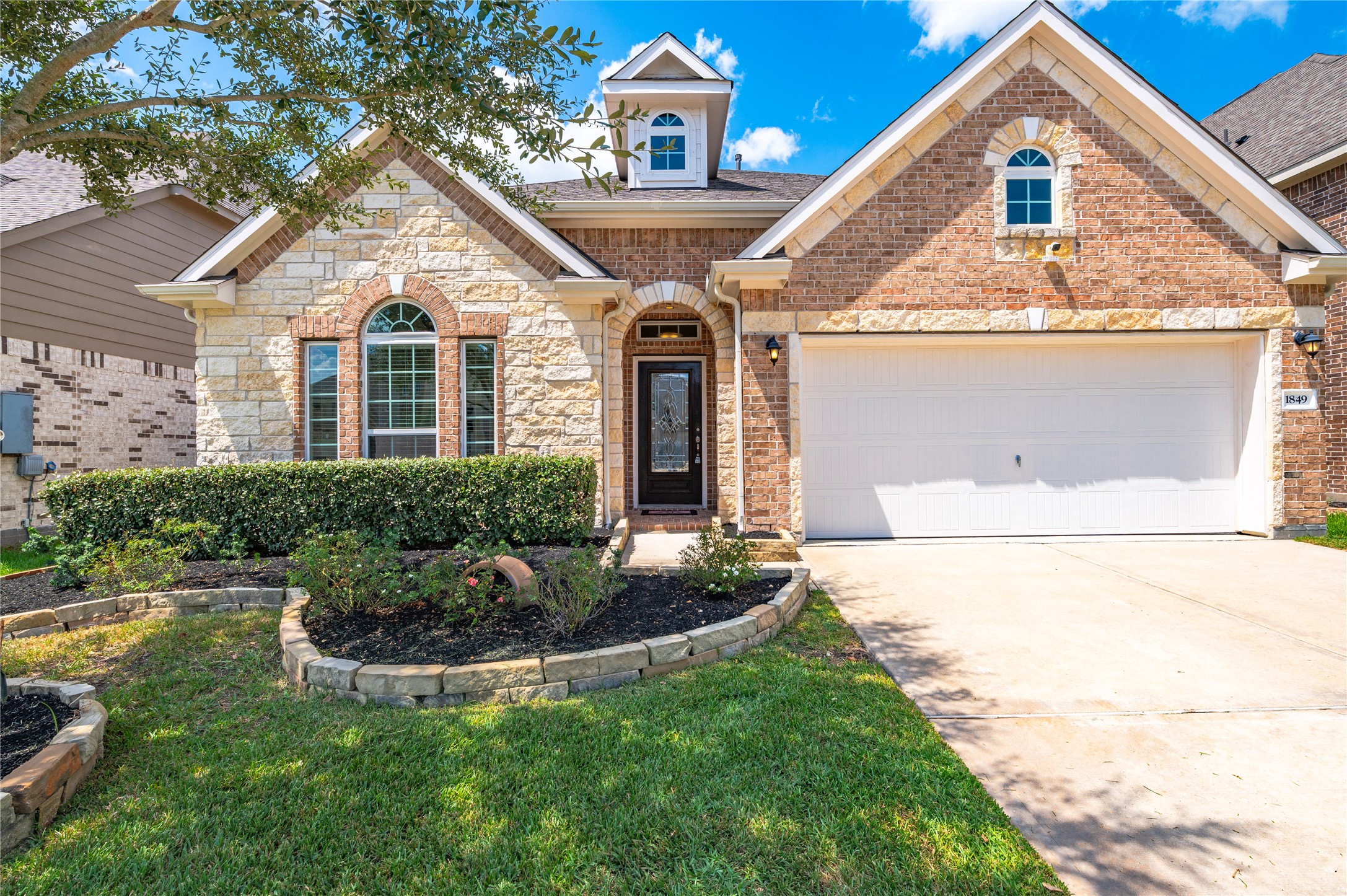 Charming brick and stone home with manicured landscaping, arched windows, and a spacious two-car garage, offering great curb appeal.