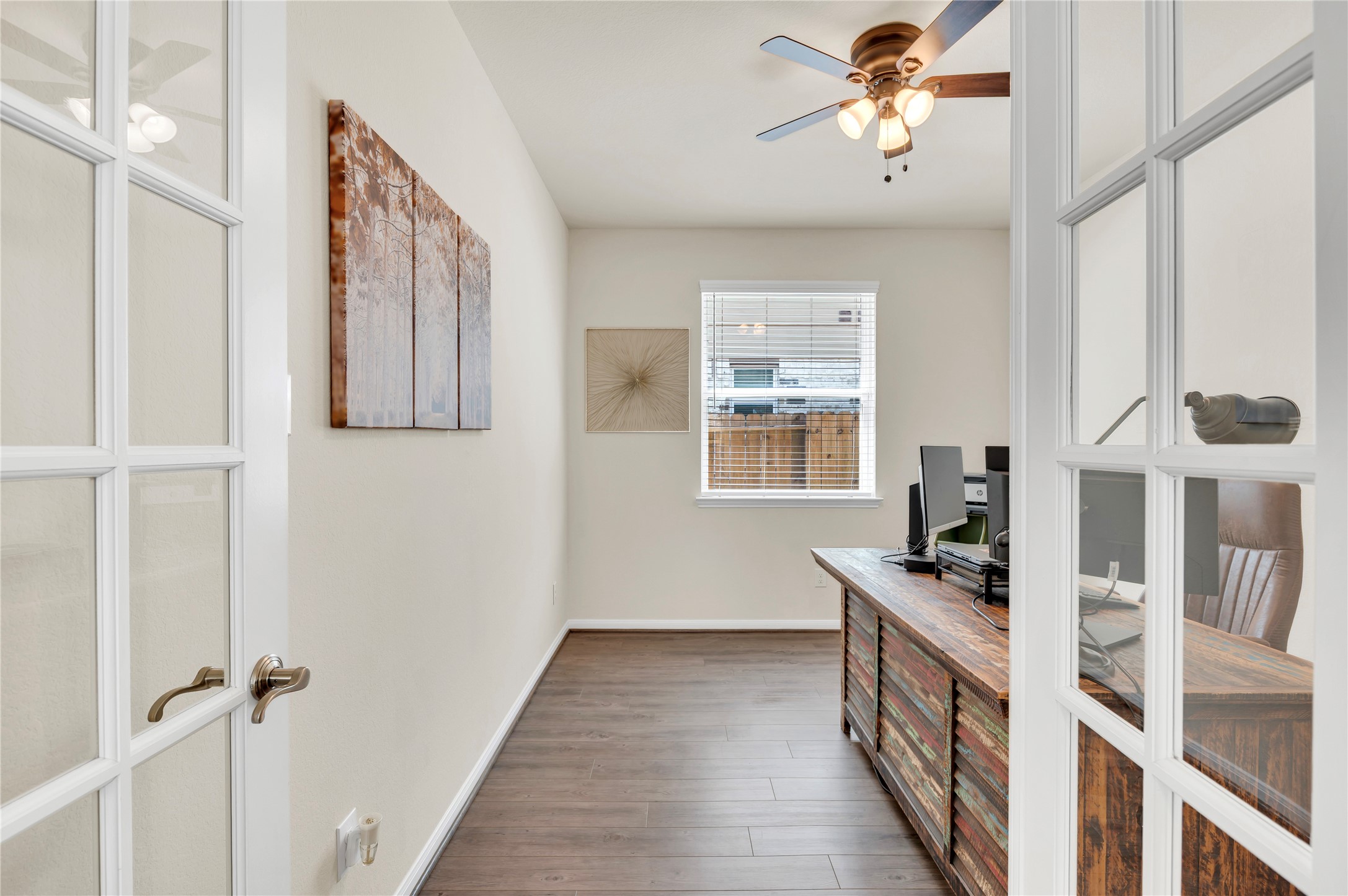 Charming home office with glass French doors, rich wood flooring, and ample natural light from a large window, creating an inviting workspace. This room also has a closet for additional storage or a 4th bedroom.
