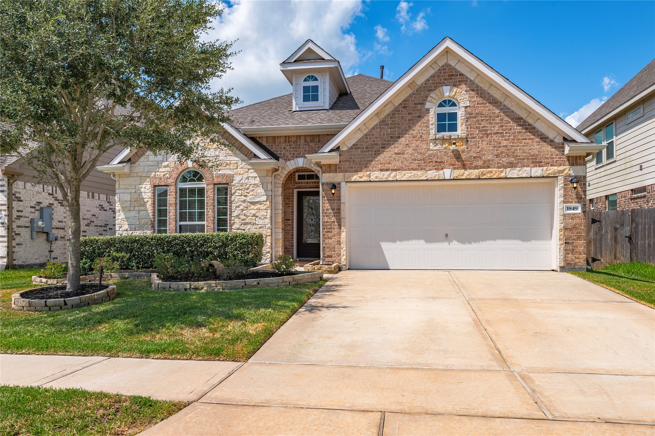 Charming brick and stone facade home with a well-maintained front yard, featuring a spacious driveway and a two-car garage.