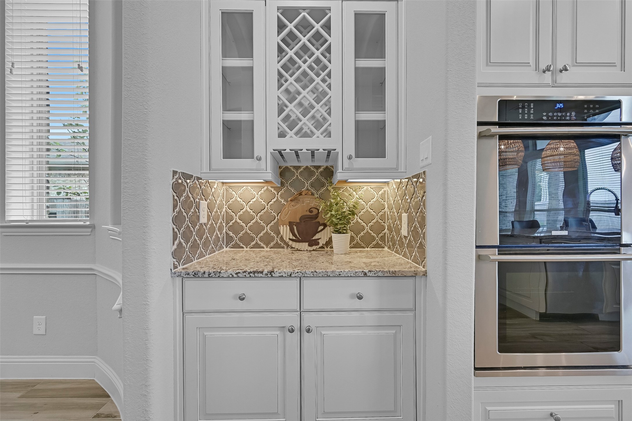 Connecting the dining room and kitchen, the butler's pantry provides additional storage and serving space with granite countertops, glass-front cabinetry, decorative wine storage, and matching arabesque tile backsplash accents.